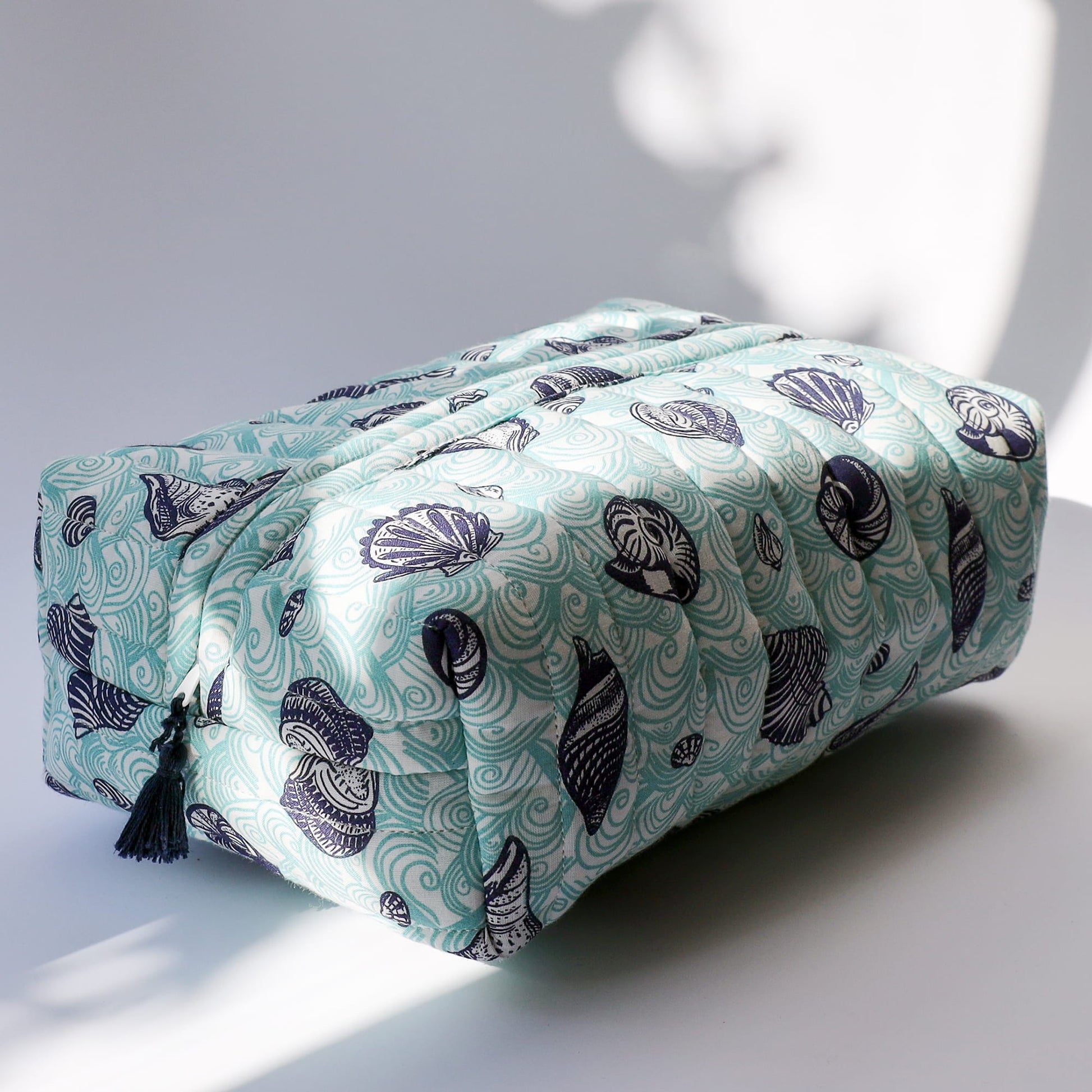 Quilted fabric wash bag with wave and shell pattern in aqua & navy on a light surface.