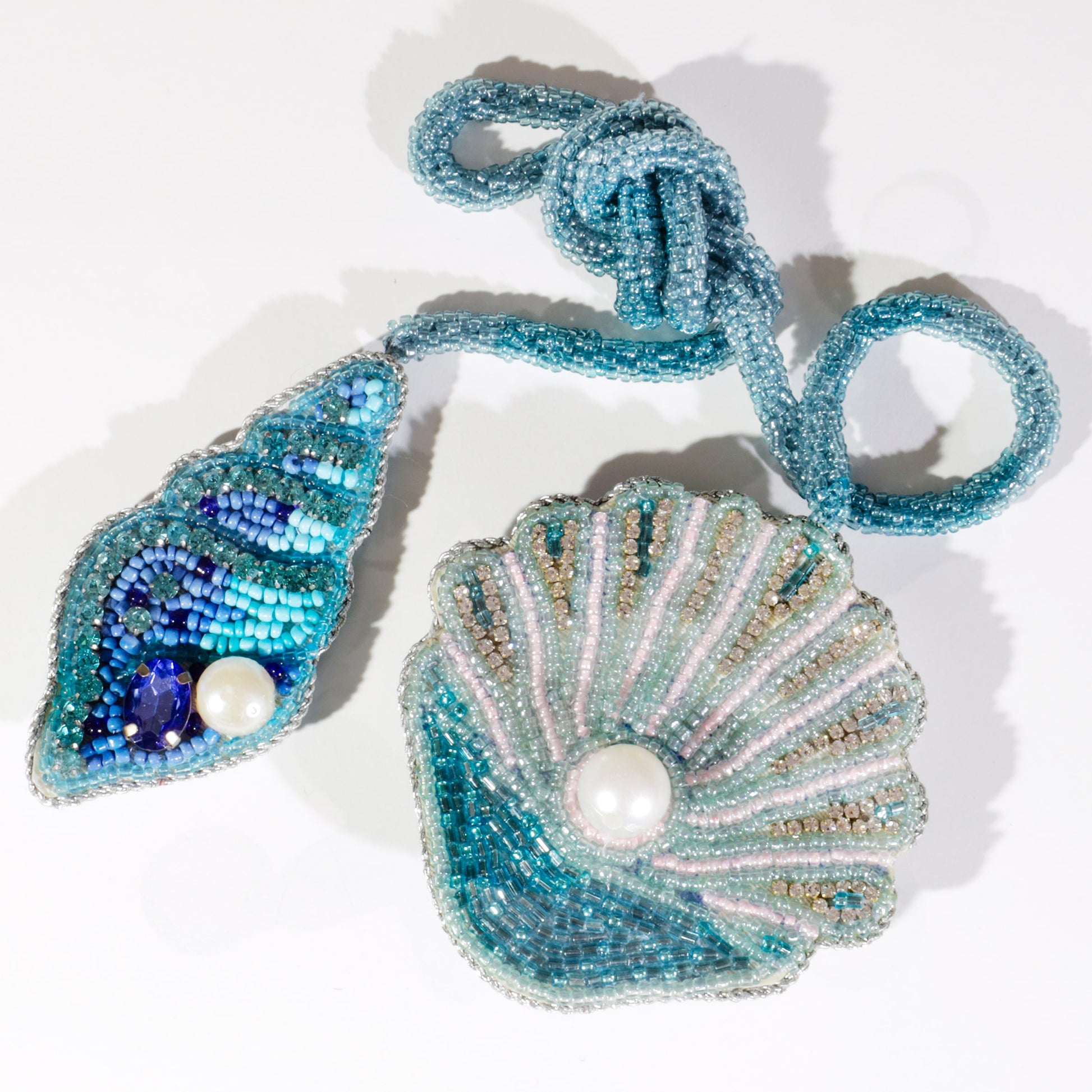 Pair of beaded shell bag charms in turquoise, blue, and gold tones with pearl and gemstone details, displayed on a white background