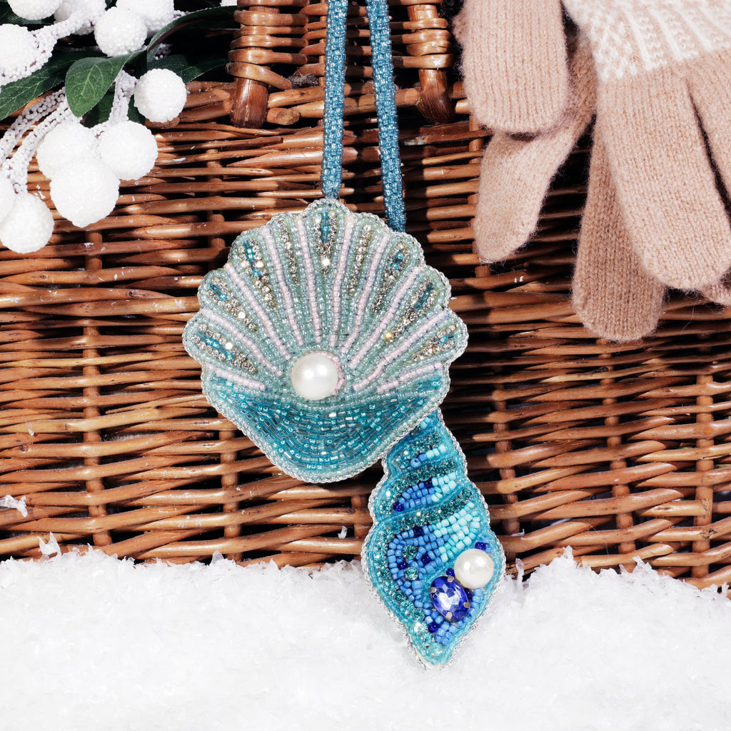 Beaded shell bag charms in shades of turquoise, blue, and gold with pearl accents hanging from a wicker basket, surrounded by snow, white berries, and wool gloves.