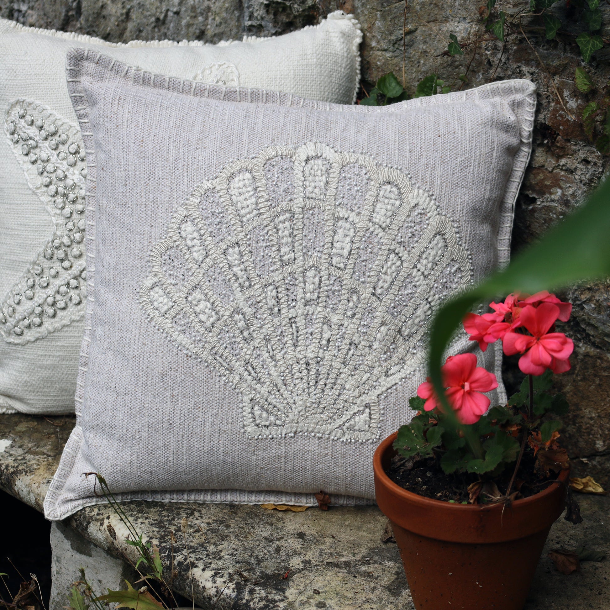 Decorative pillow with shell pattern next to a potted plant on a stone surface