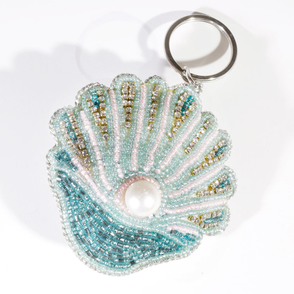 A beaded shell keyring decorated with turquoise, pink, and gold beads and a central pearl detail, displayed against a white background.