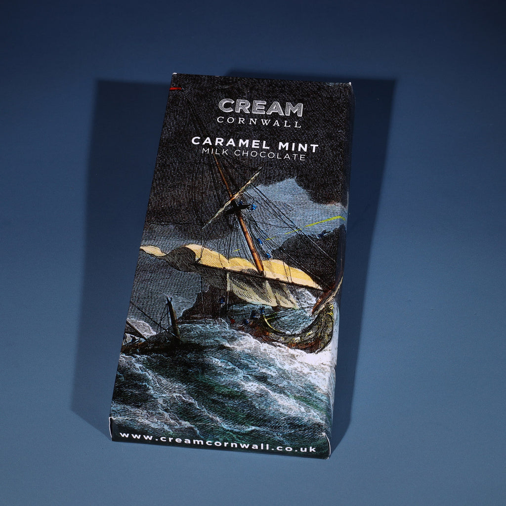 Caramel milk chocolate bar wrapped in a shipwreck scene etching. The bar has been photographed on a graduated blue background.