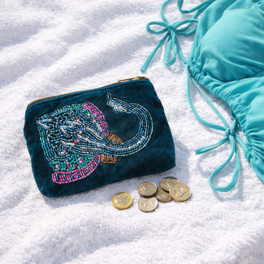 Beaded coin purse with skate design on teal velvet, laid on white beach towel with coins & bikini.