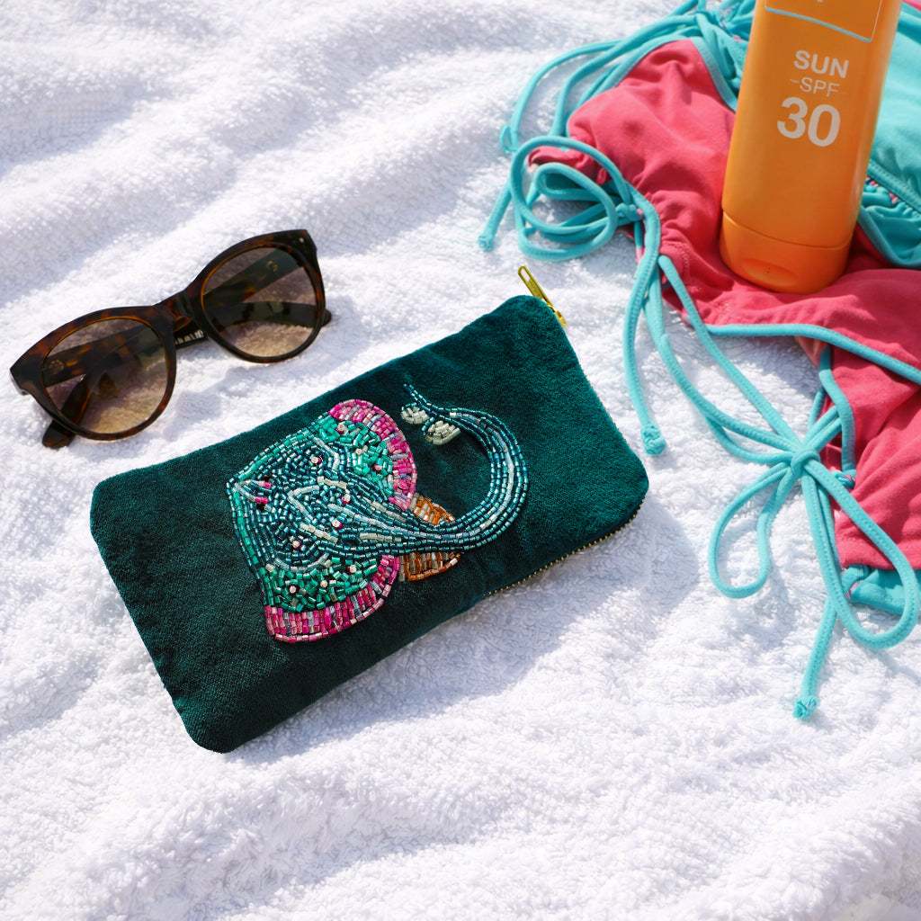 teal beaded glasses case with sunglasses, sunscreen, and bikini on a sandy background