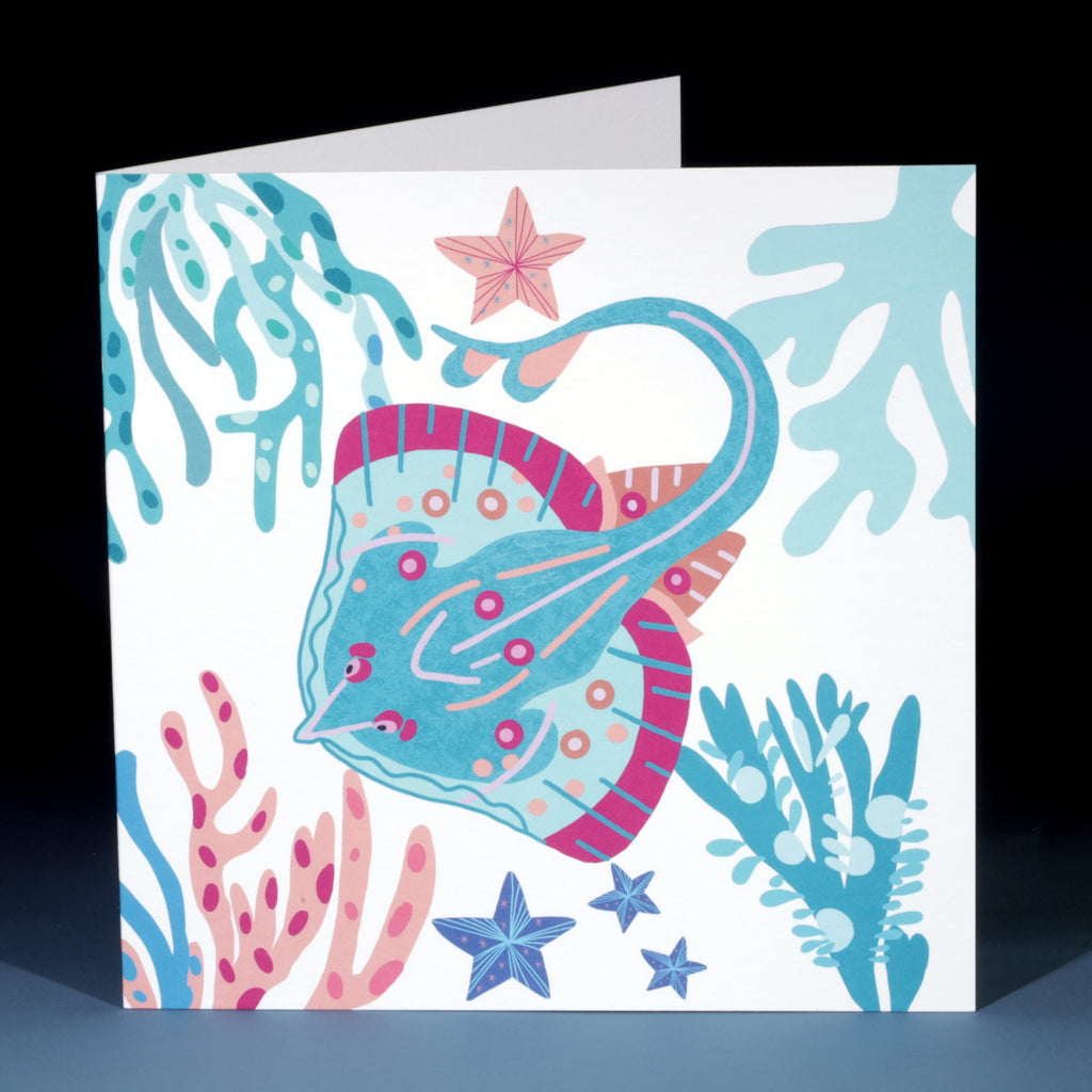Front of a greeting card featuring a vibrant underwater illustration of a blue and pink skate surrounded by coral, seaweed, and starfish in shades of teal, peach, and navy on a white background.