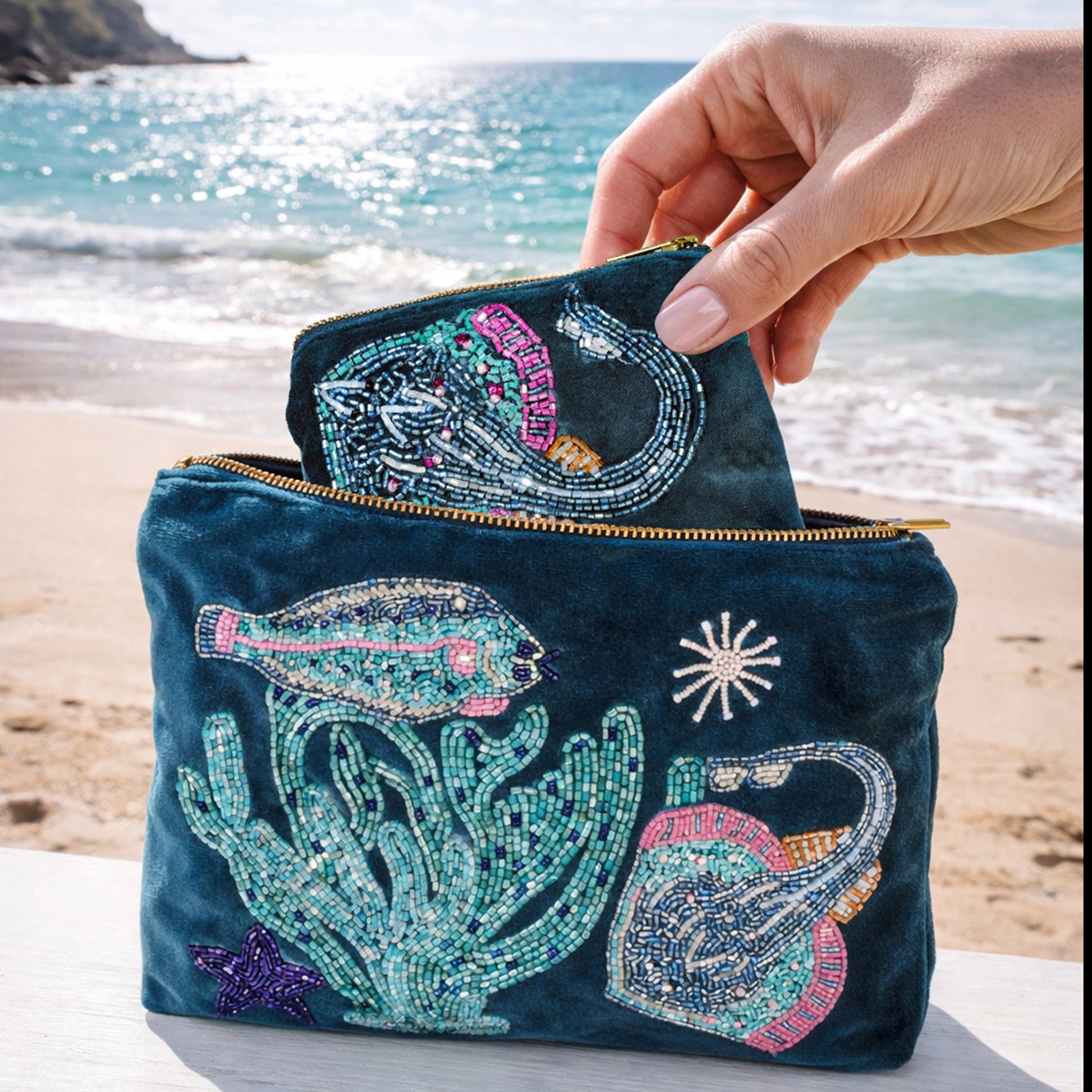 Embroidered pouch with ocean-themed designs held by a hand on a beach.