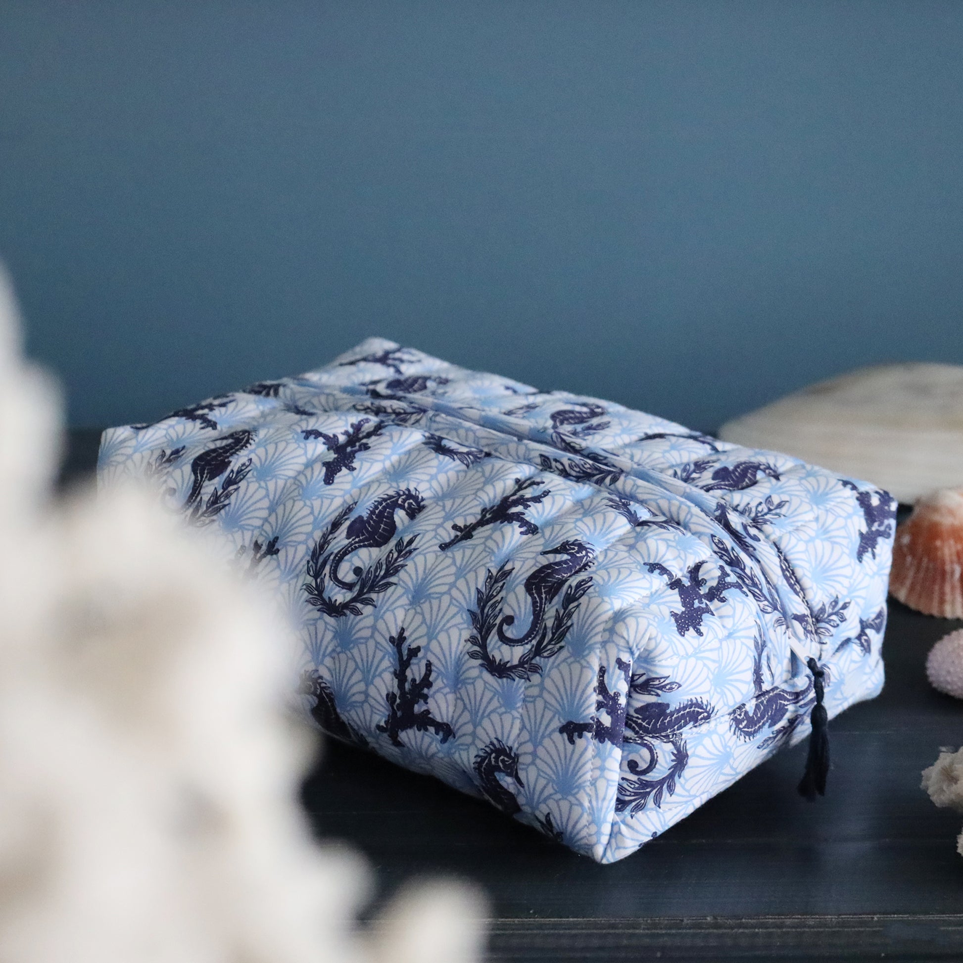 Blue and white patterned seahorse & coral toiletry bag on a dark surface with a blue wall background.