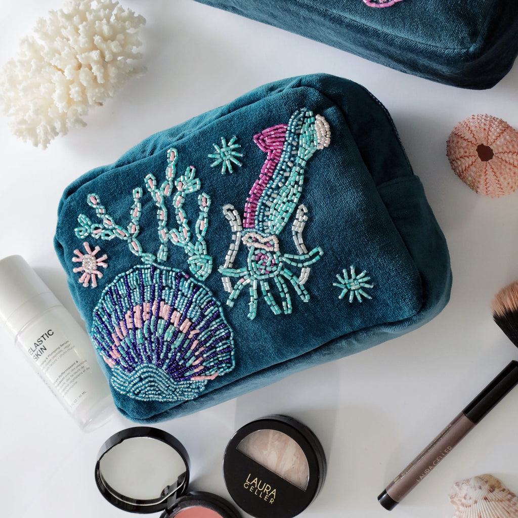 Teal embroidered pouch with sea-themed design on a white surface with makeup items.