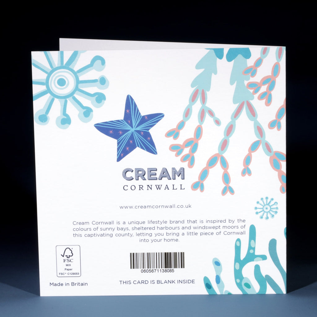 The back of a Cream Cornwall greeting card featuring pastel illustrations of a blue starfish, pink coral branches, and abstract marine motifs. The text includes branding, a description of the inspiration behind the design, and a barcode. The card is noted as being blank inside and made in Britain.
