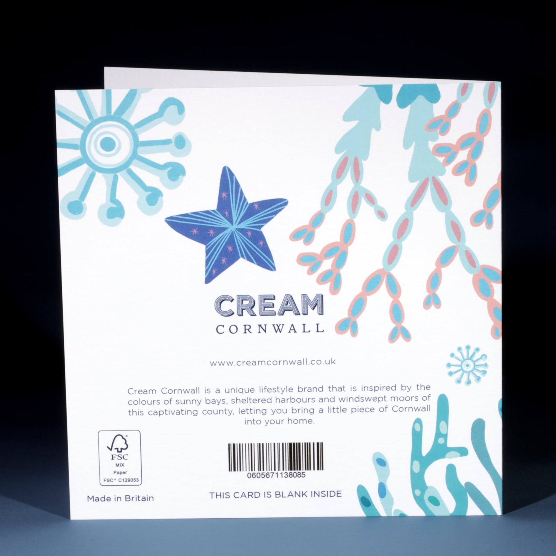 The back of a Cream Cornwall greeting card featuring pastel illustrations of a blue starfish, pink coral branches, and abstract marine motifs. The text includes branding, a description of the inspiration behind the design, and a barcode. The card is noted as being blank inside and made in Britain.