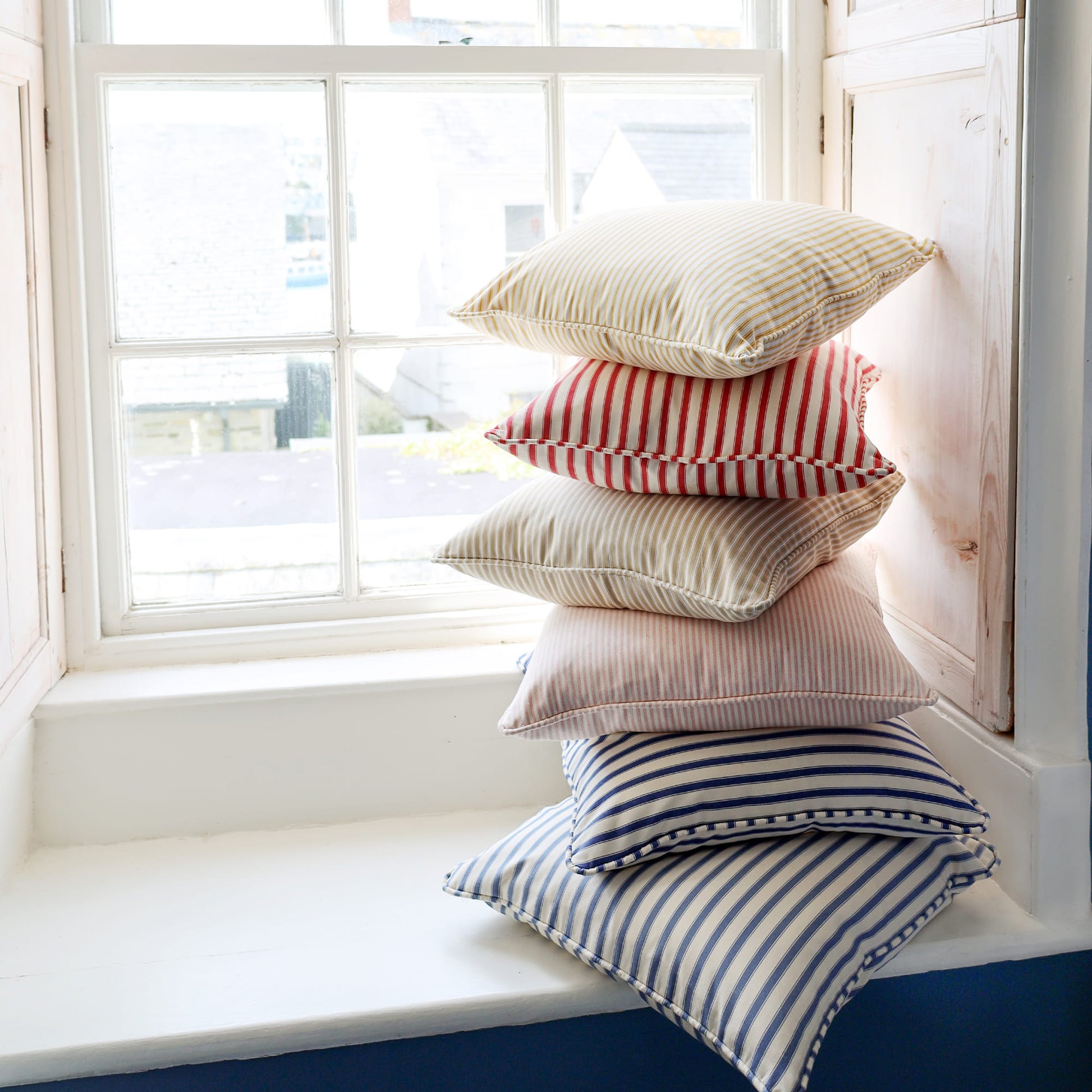 Stack of colorful pillows on a windowsill with a view outside.