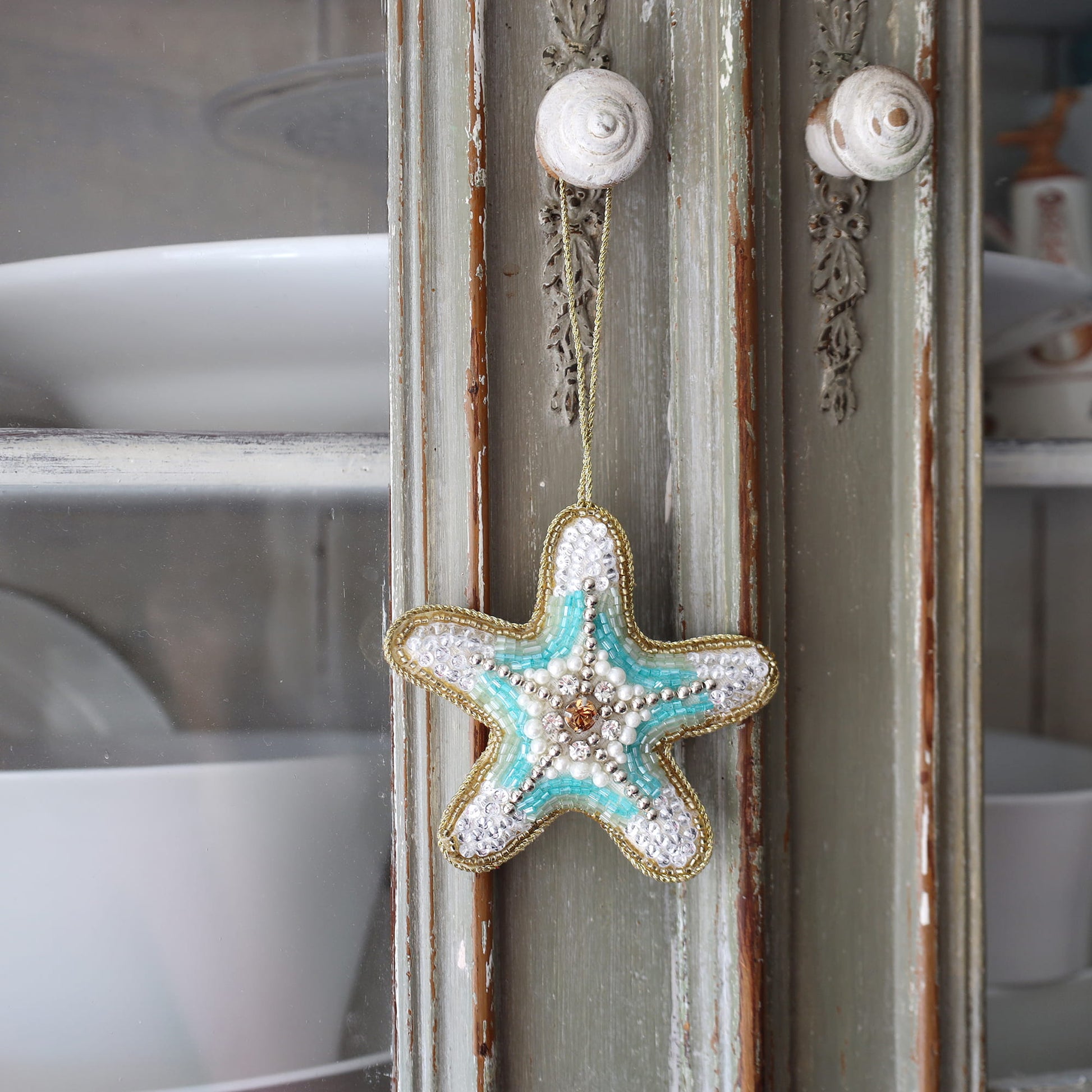 Decorative starfish ornament hanging on a textured wall with shell accents.