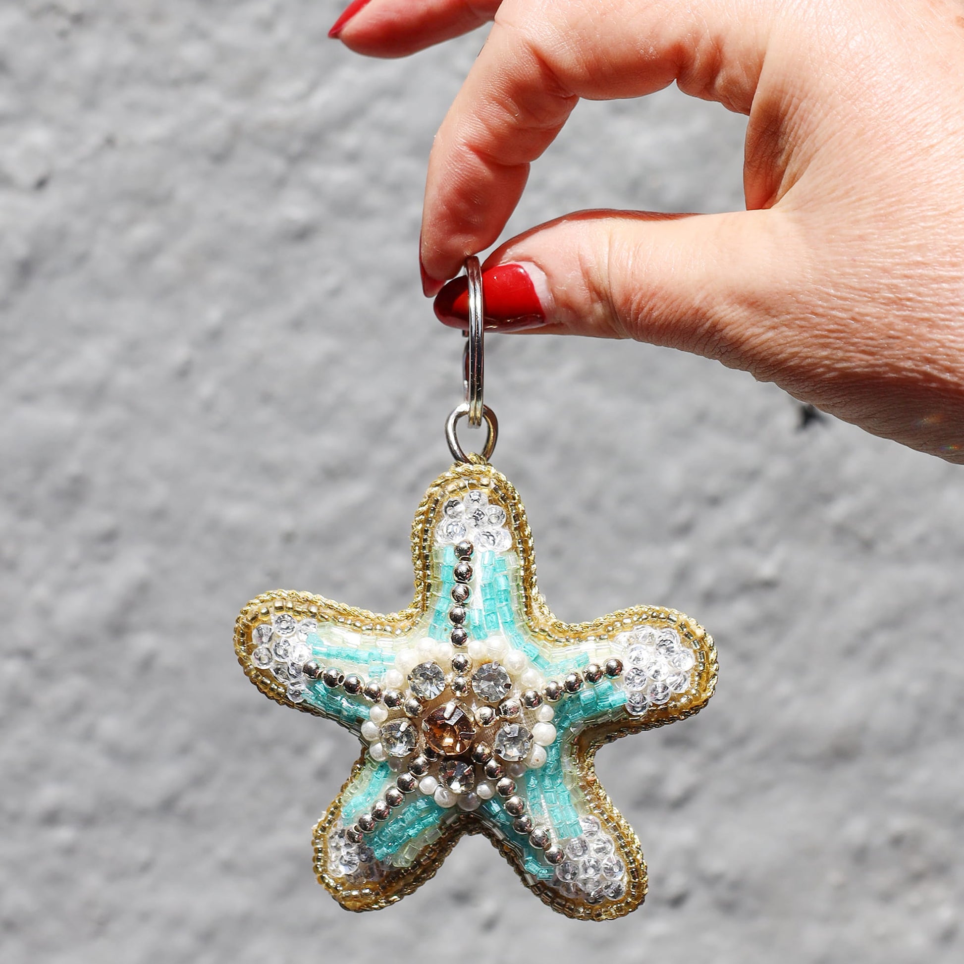 Starfish-shaped keychain with decorative elements held by a hand against a gray background