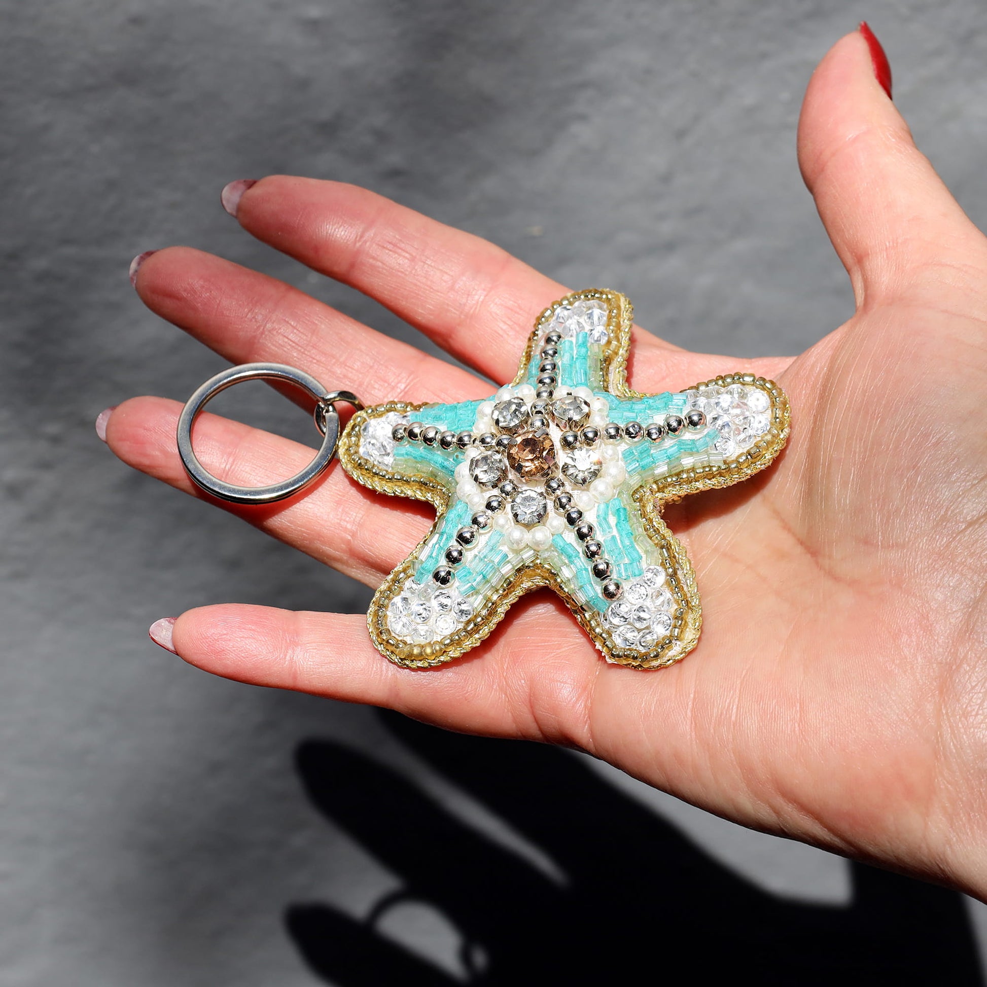 Starfish-shaped keychain with decorative elements held in a hand against a gray background
