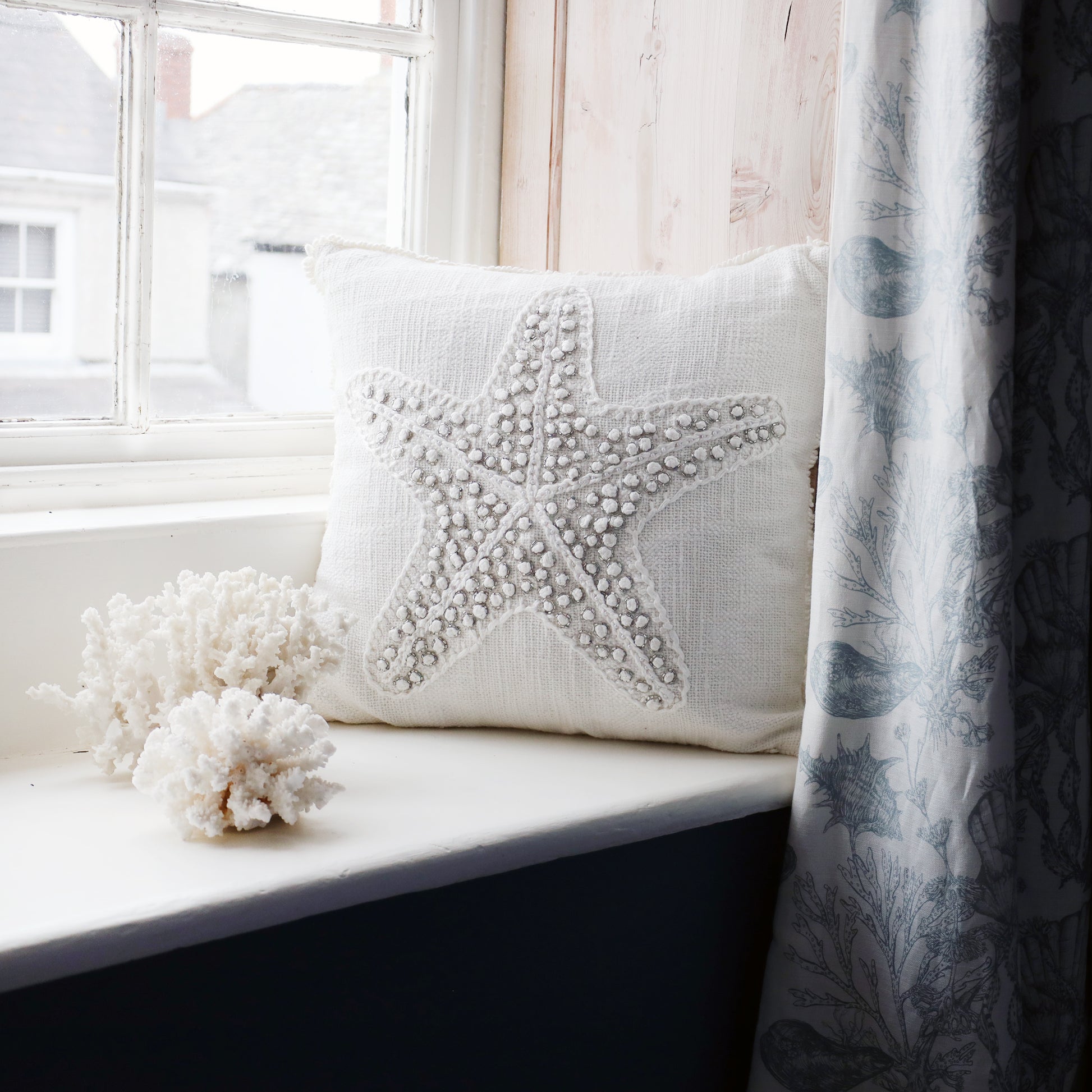 Decorative pillow with starfish design on a windowsill next to a curtain