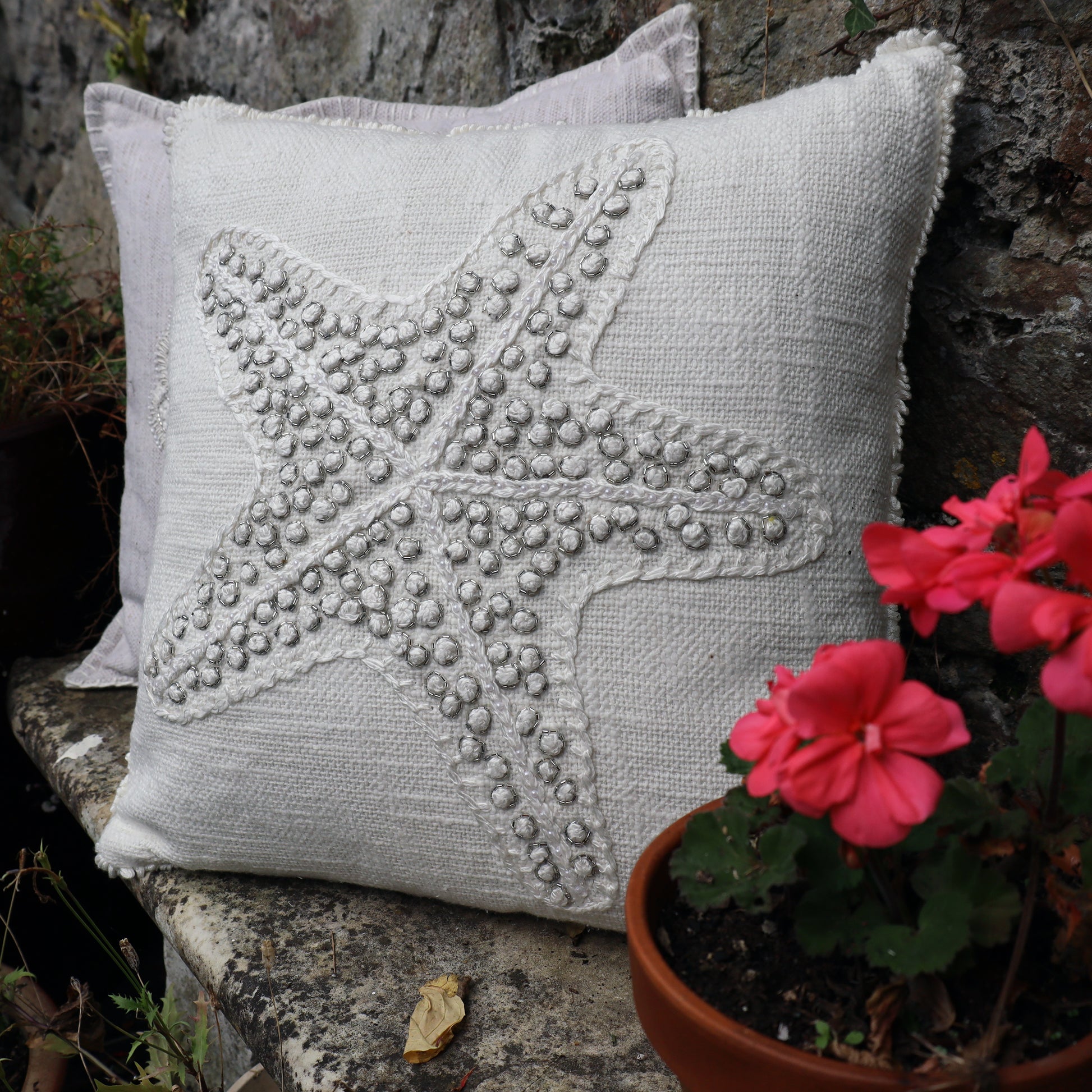 Decorative pillow with starfish design on a stone surface with flowers.