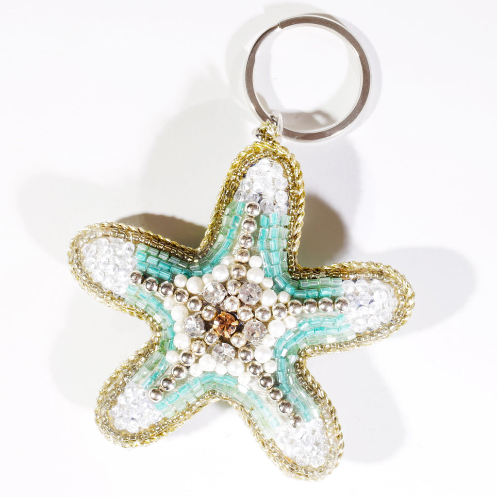 A starfish-shaped beaded keyring with turquoise, white, and gold beads and a sparkling gem at the centre, displayed on a white background.