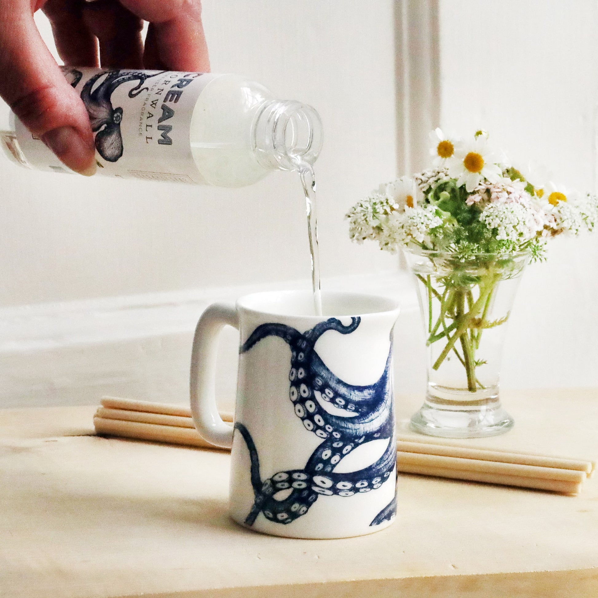 Mini Jug with octopus design on with reeds and small posy of flowers behind with a bottle of Storm Brewing room diffuser oil being poured into the jug.