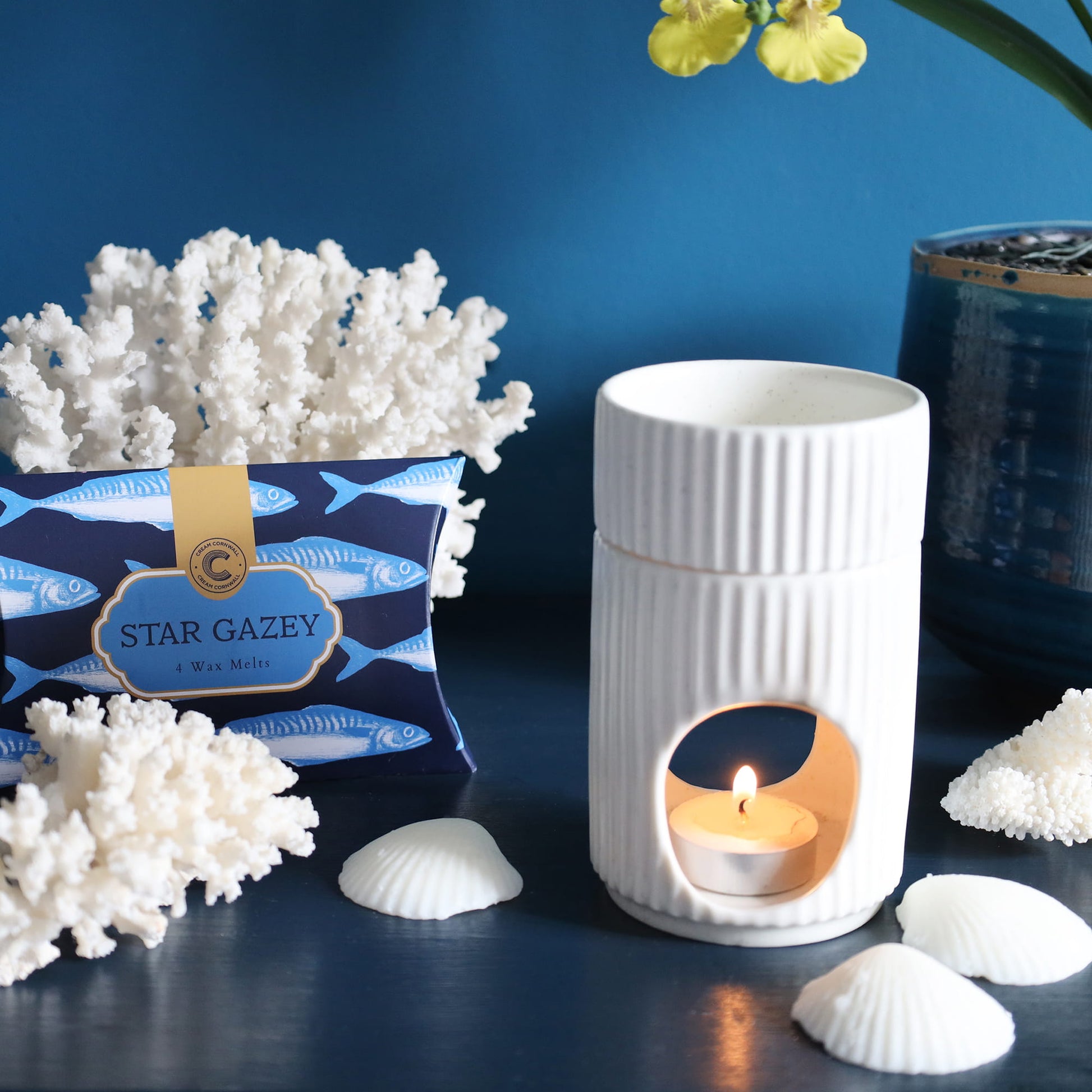 White textured wax melter with lit candle surrounded by decorative elements on a blue background