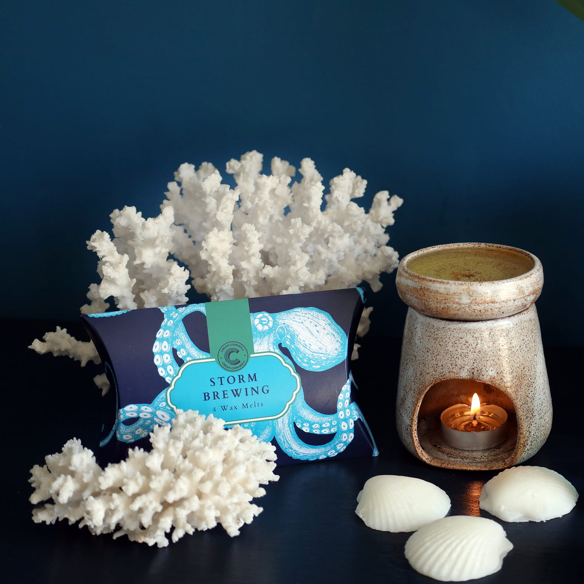 Wax melt container labeled 'Storm Brewing' with a ceramic warmer and decorative elements on a dark background.
