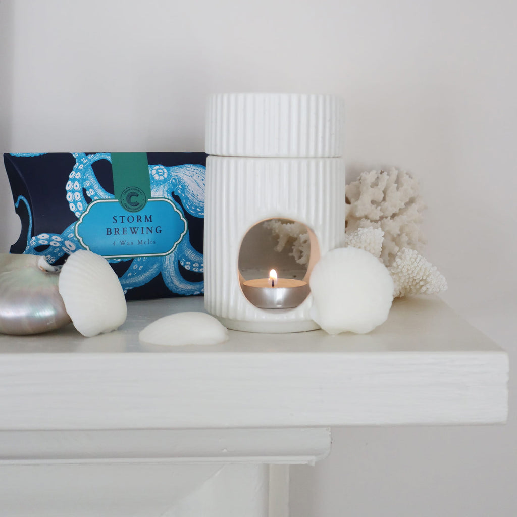 White ceramic lantern with candle, decorative stones, and a card on a white surface.