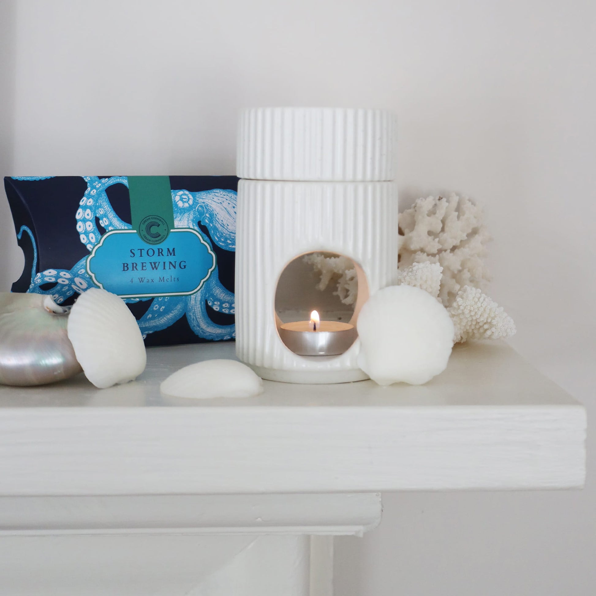 White ceramic lantern with candle, decorative stones, and a card on a white surface.