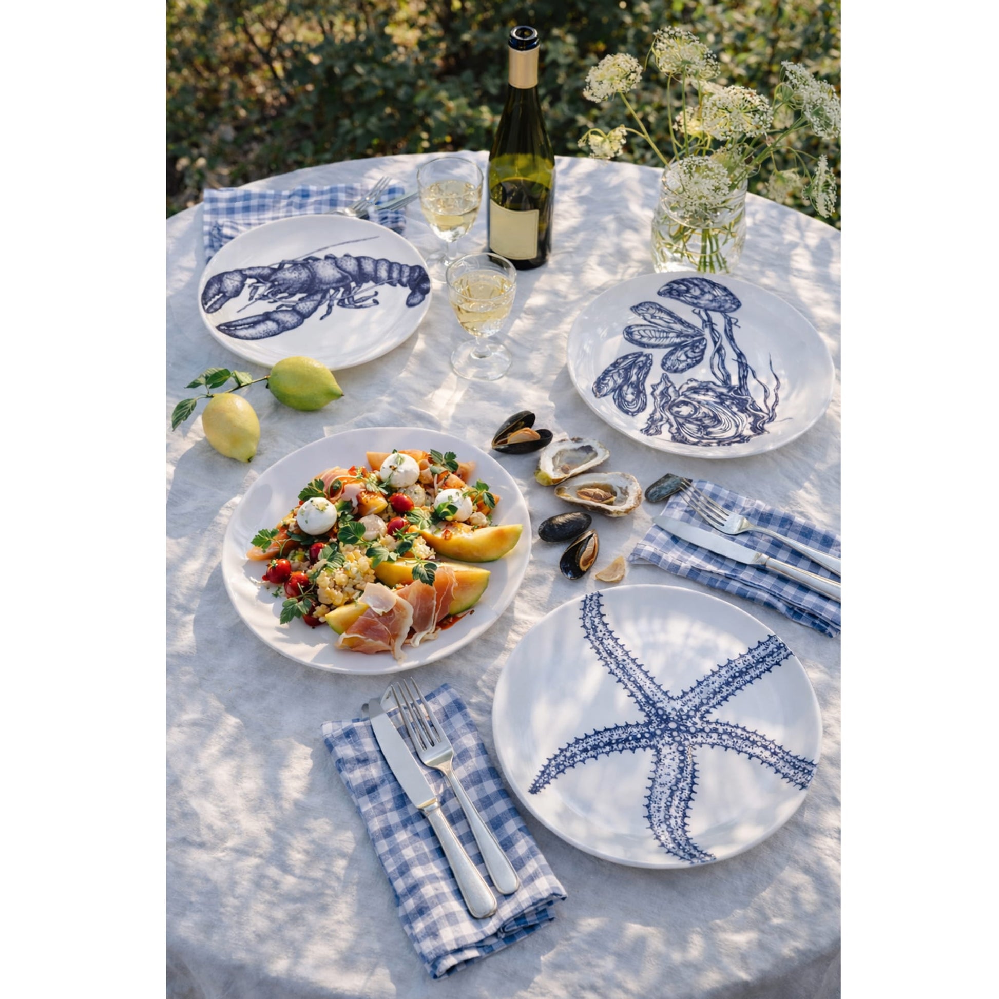 Outdoor dining table setting with blue and white plates featuring sea-themed designs, food, and wine.