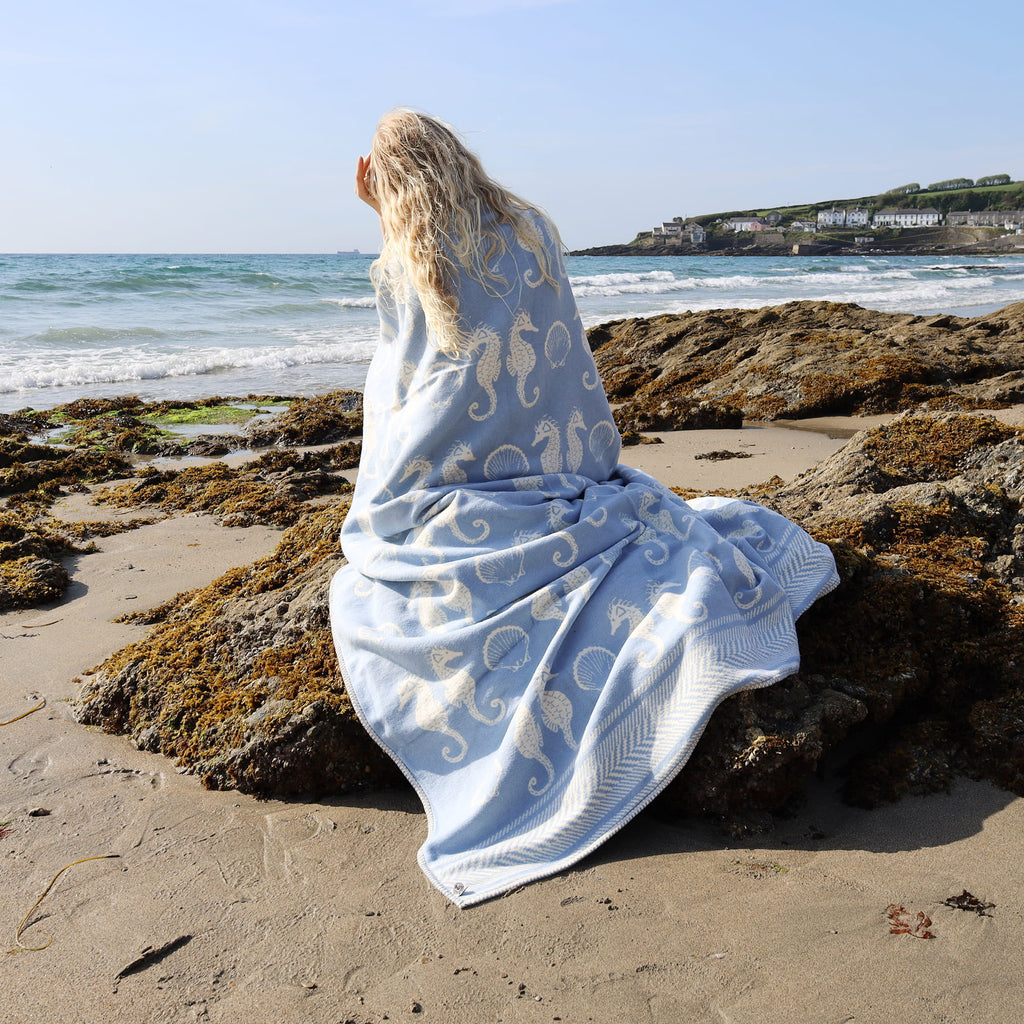 Person sitting on a rocky beach with a patterned blanket draped over them