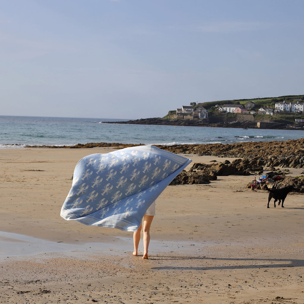 Person standing on a beach with a large white towel draped over them, facing the ocean.