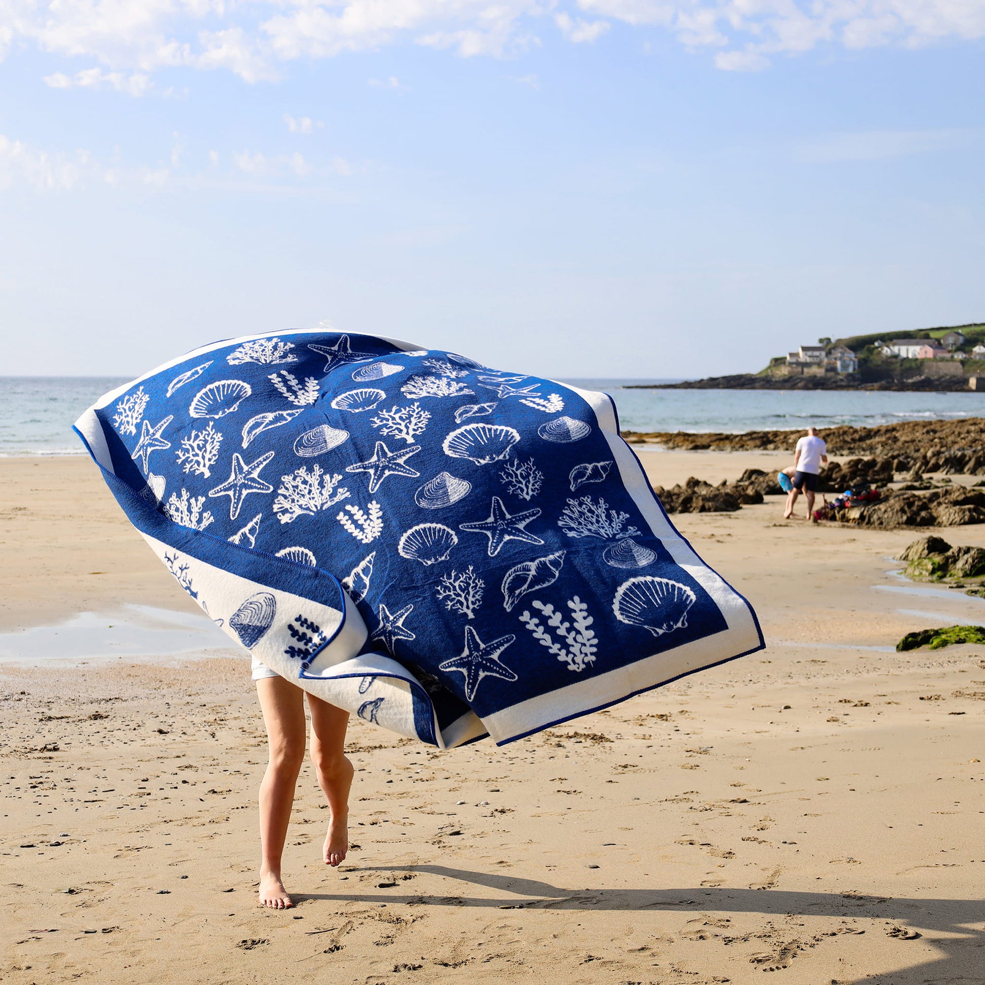 Person holding a blue towel with white sea-themed design on a beach
