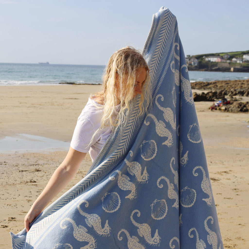 Woman holding a blue towel with white patterns on a beach
