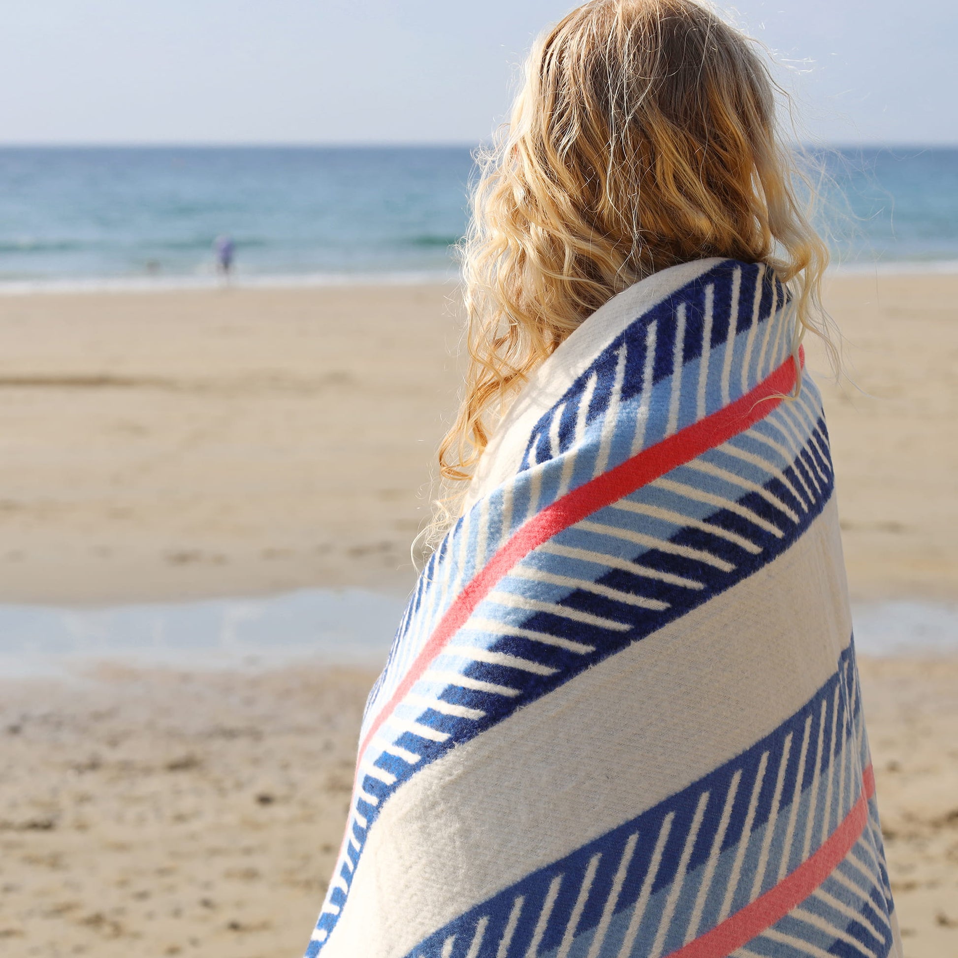 Person wrapped in a striped towel on a beach with ocean view