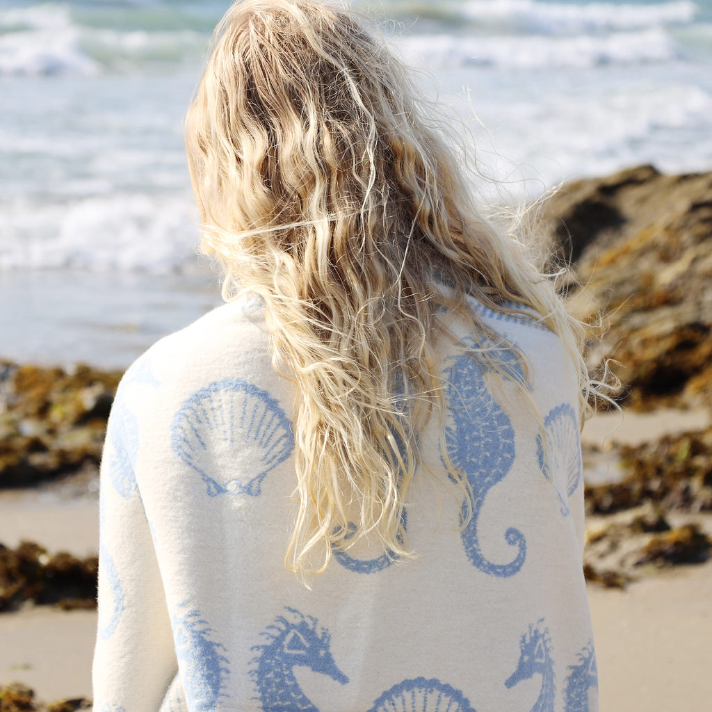 Person wearing a white cardigan with blue patterns on a beach