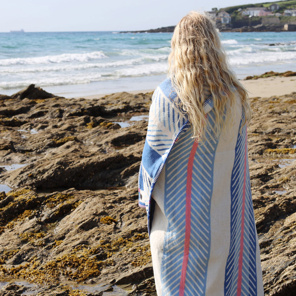 Person wrapped in a striped towel on a rocky beach with ocean view