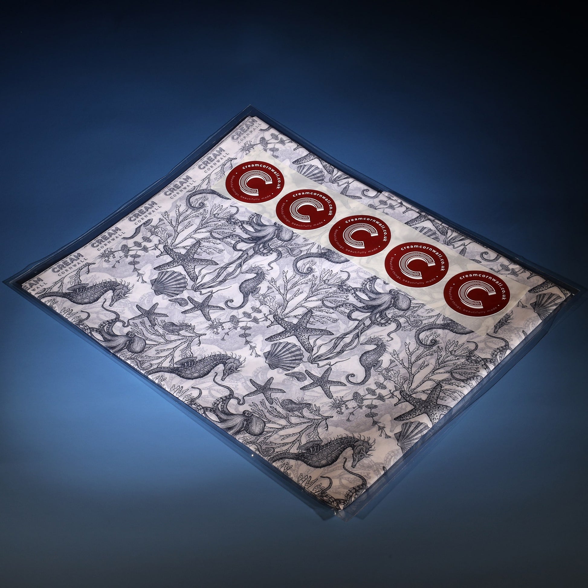 Pack of printed tissue paper with navy sea creatures and seaweed on, folded in cellophane pack with 5 cream cornwall round red sticks.