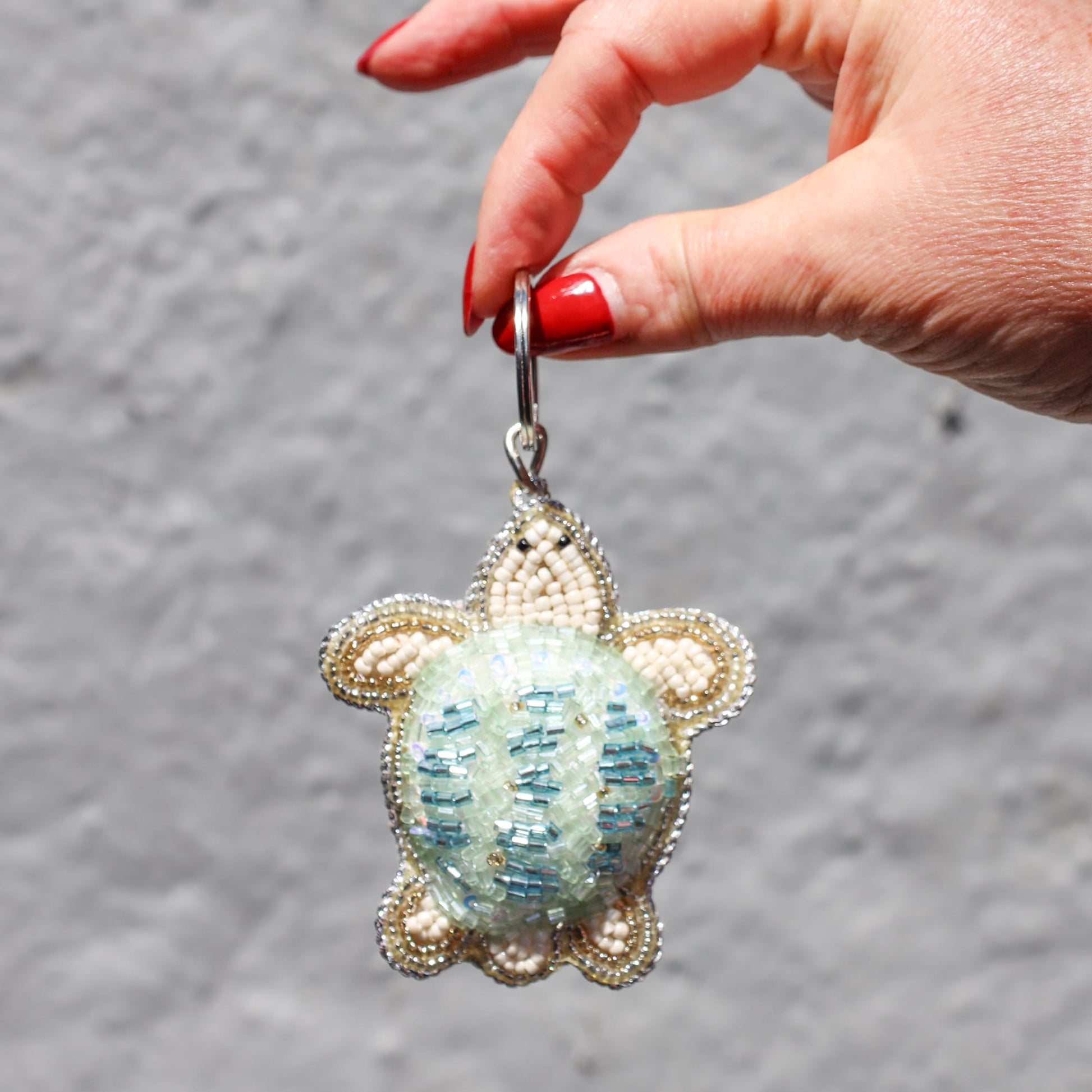 Hand holding a turtle-shaped keychain with beadwork against a gray background