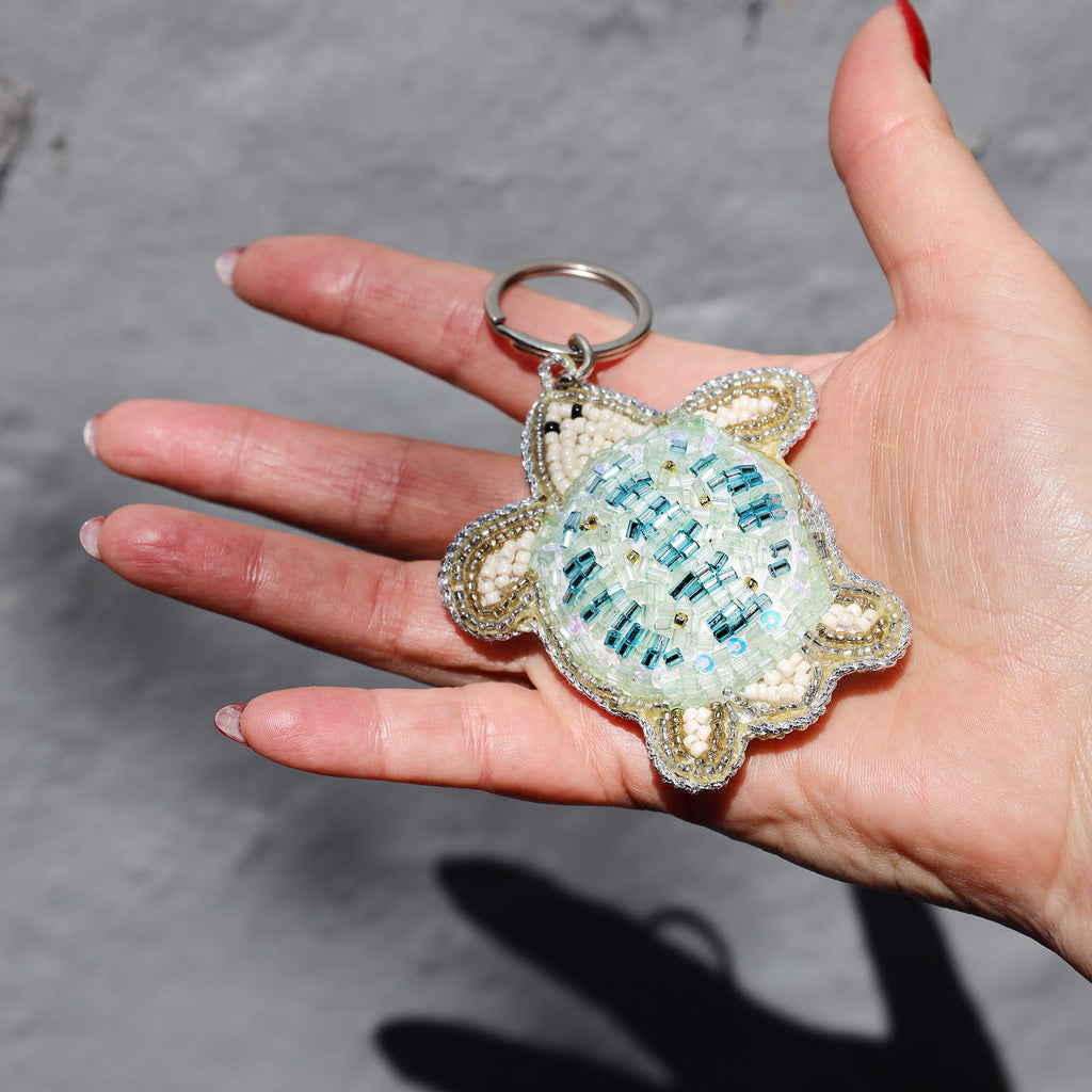 Hand holding a decorative turtle keychain with a gray background