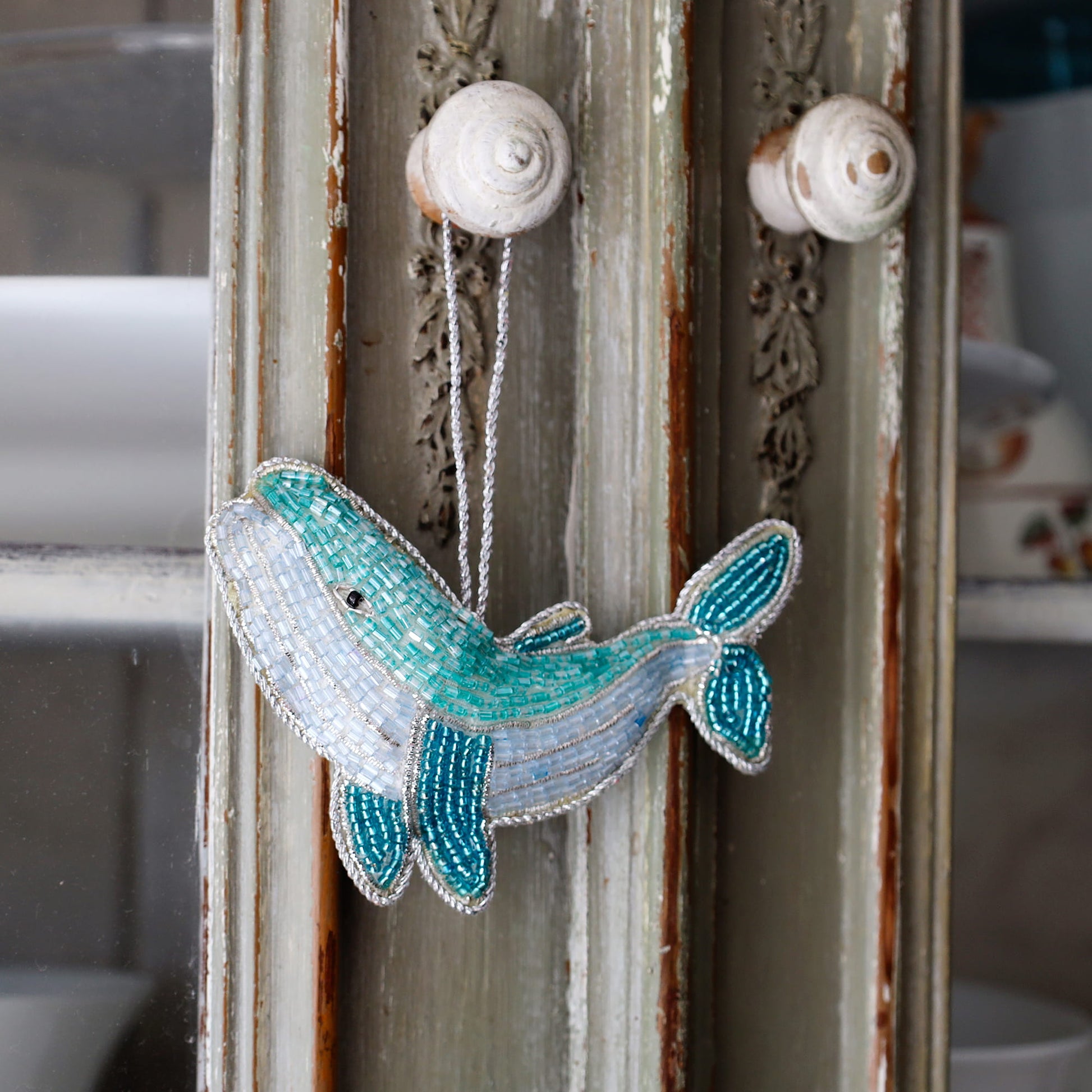 Decorative whale ornament with beads hanging on a rustic wooden door.