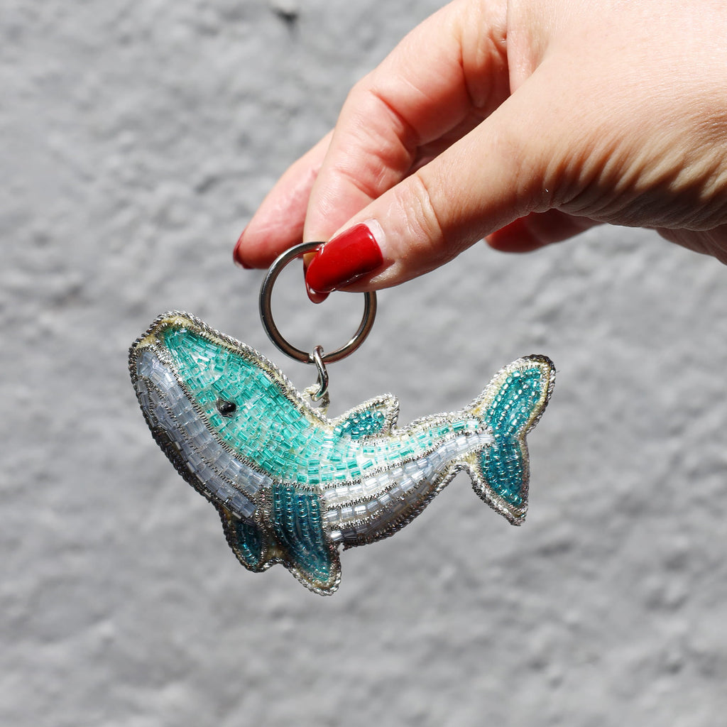 Hand holding a beaded whale keychain against a gray background
