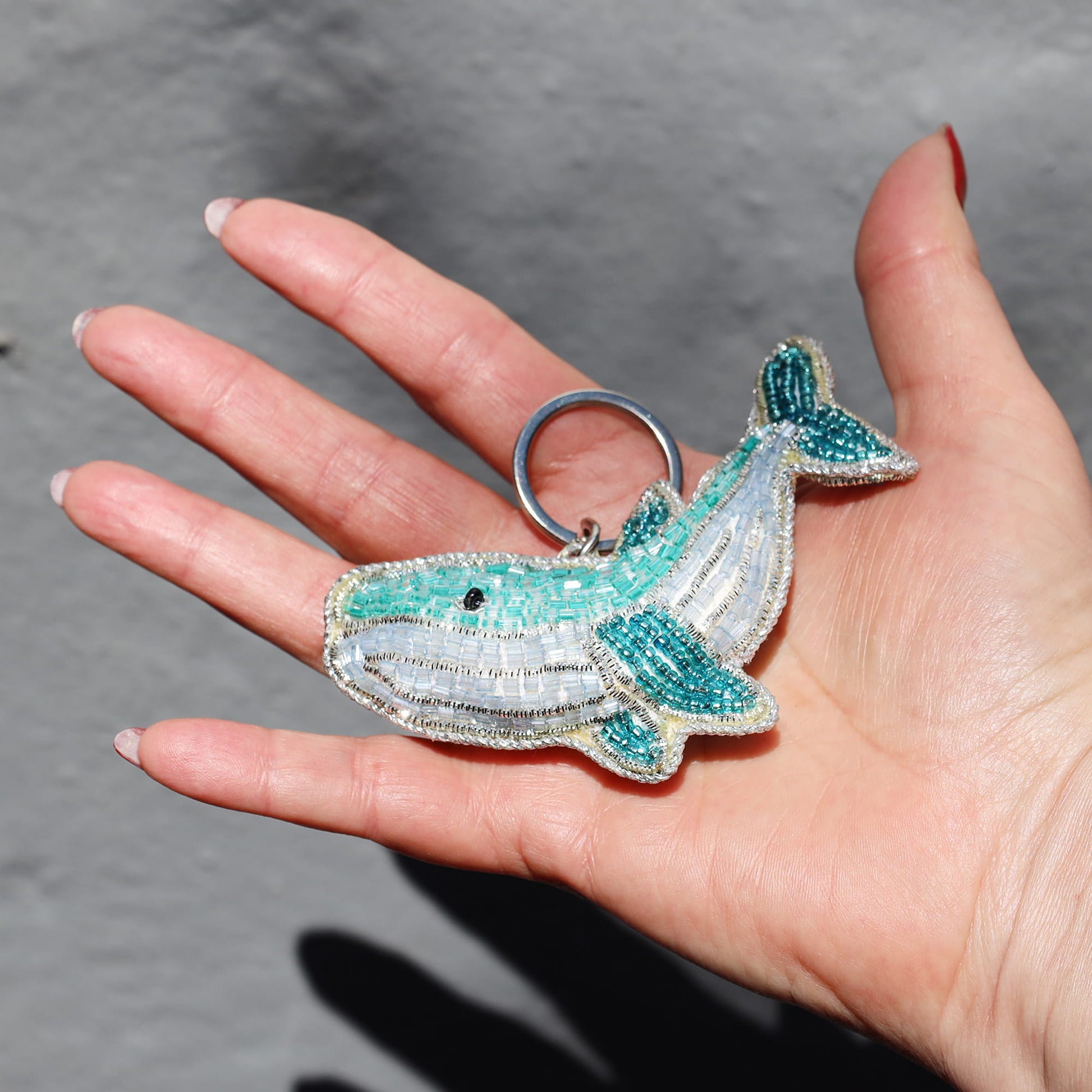 Hand holding a beaded whale keychain against a gray background