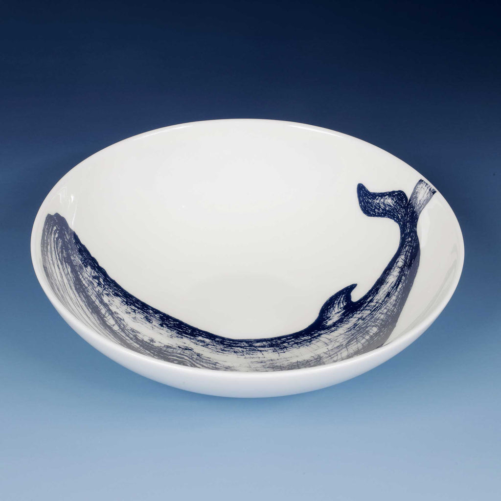 A white ceramic bowl featuring a dark blue hand-painted whale design along the inner rim, set against a blue gradient background.