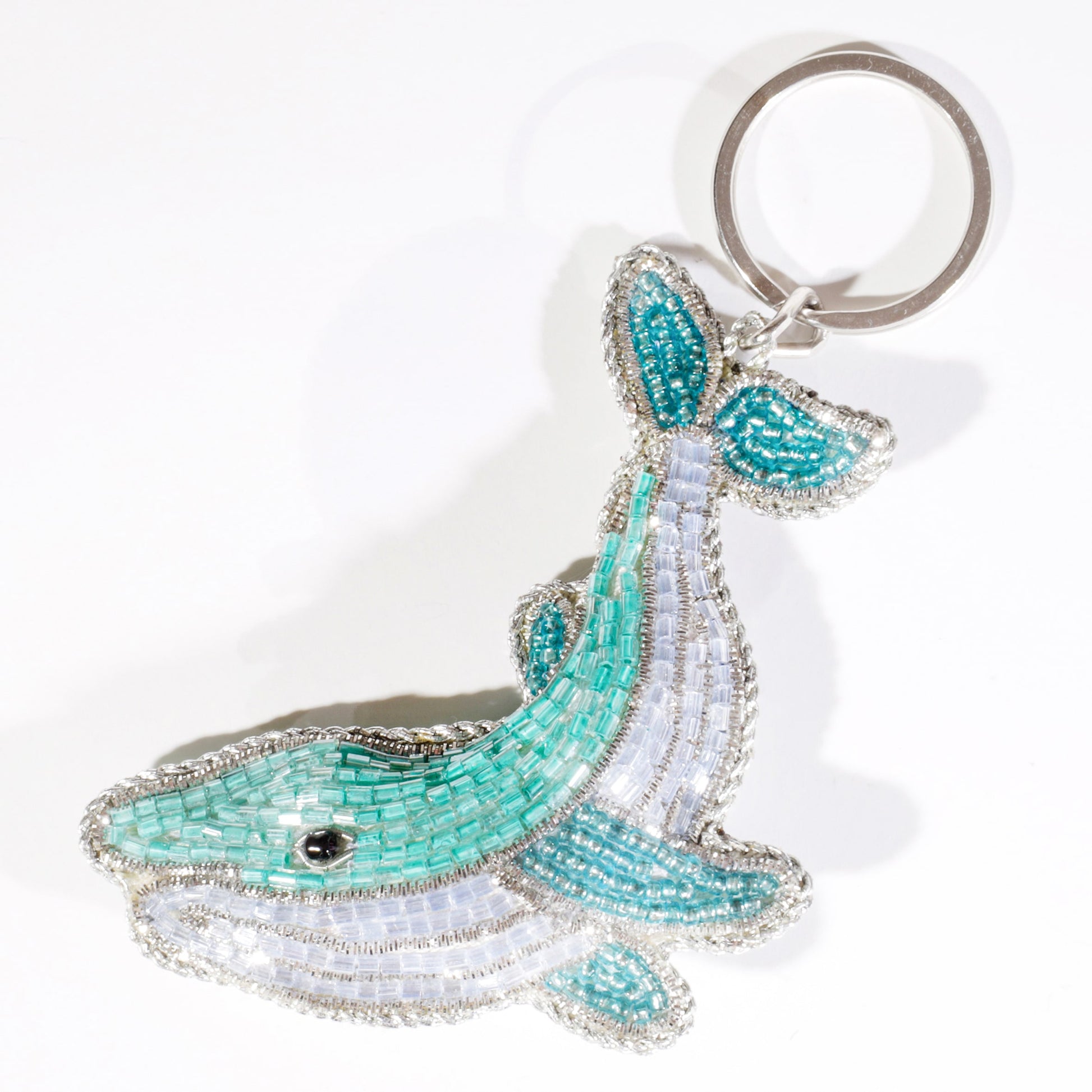 A beaded whale keyring in shades of turquoise, white, and silver, with intricate detailing and a silver keyring attachment.