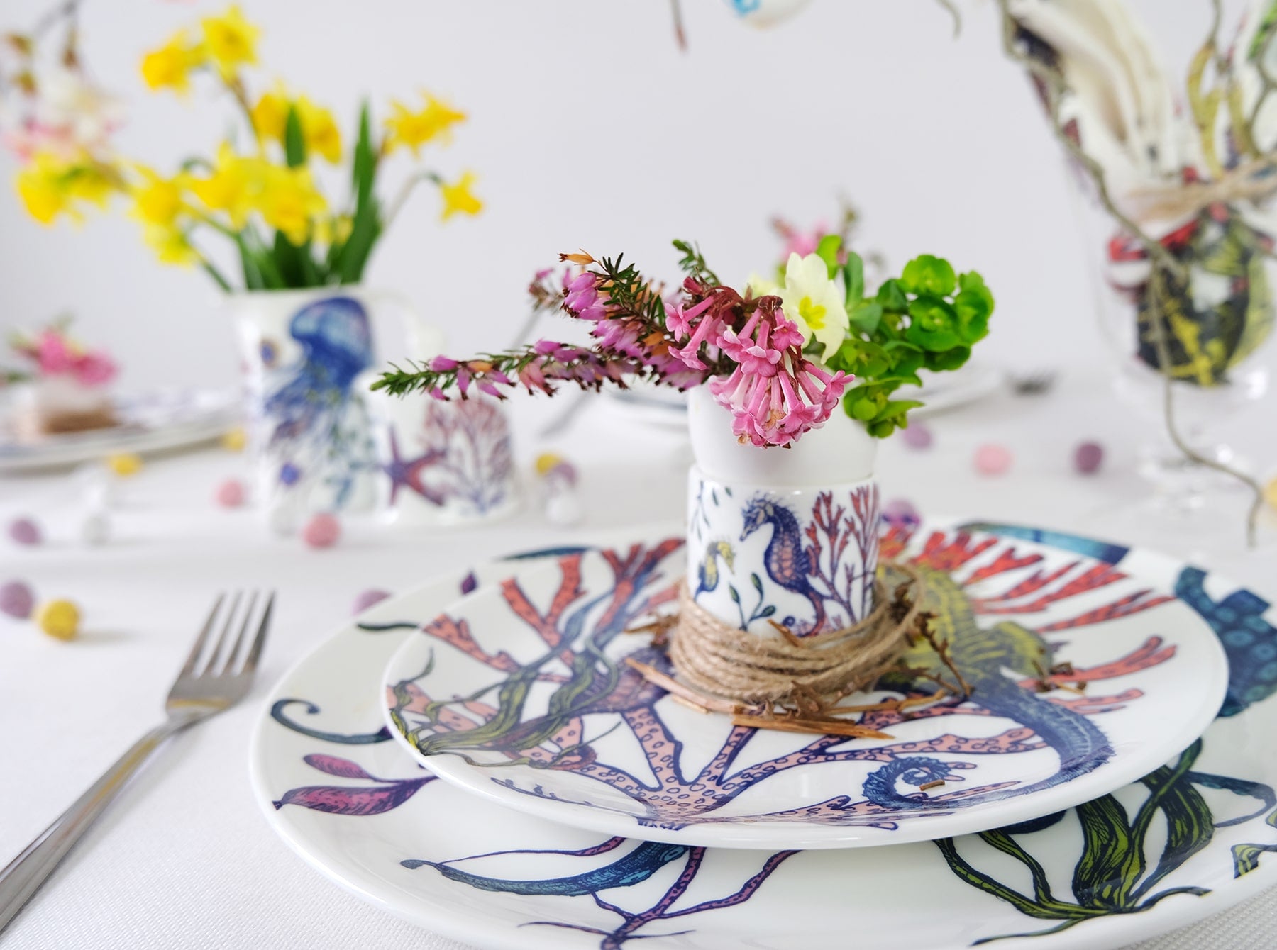 Bone China White plate with hand drawn illustration our Octopus Reef in various colours.A matching side plate and reef egg cup is placed on top.In the background are other pieces of the Reef tableware