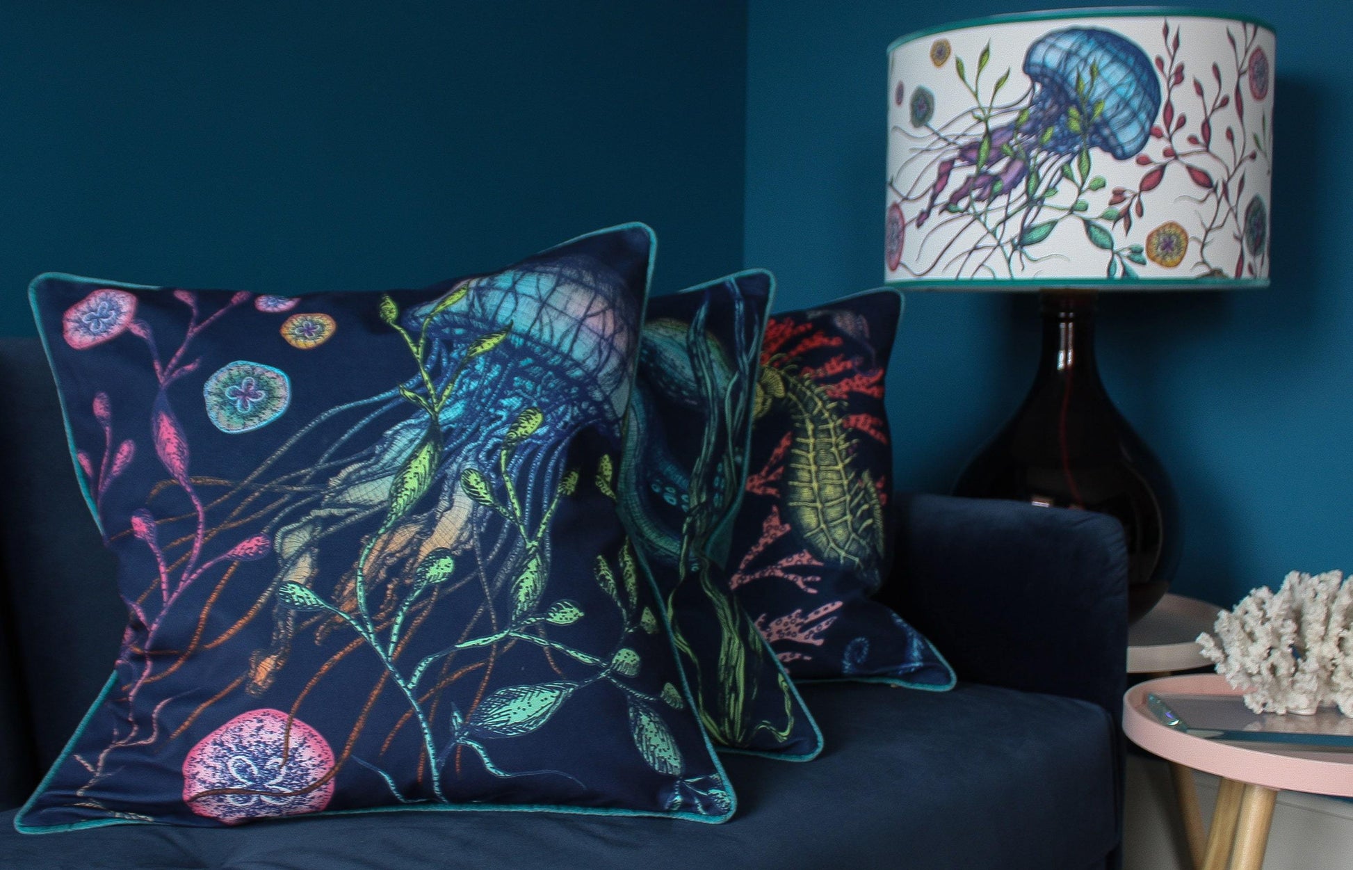 Canyons Reef White Lampshade With Jellyfish Design on a blue lampbase behind a navy sofa with reef cushions placed on it.