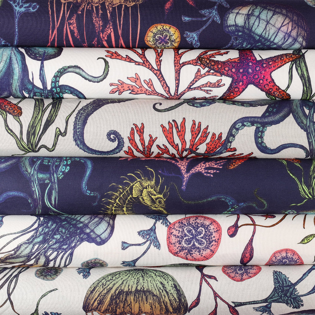 A neatly stacked bundle of fabric rolls featuring Cream Cornwall's Reef collection. The designs are inspired by marine life, showcasing detailed illustrations of jellyfish, seaweed, seahorses, octopuses, starfish, and coral in rich hues of navy, teal, red, and soft cream.