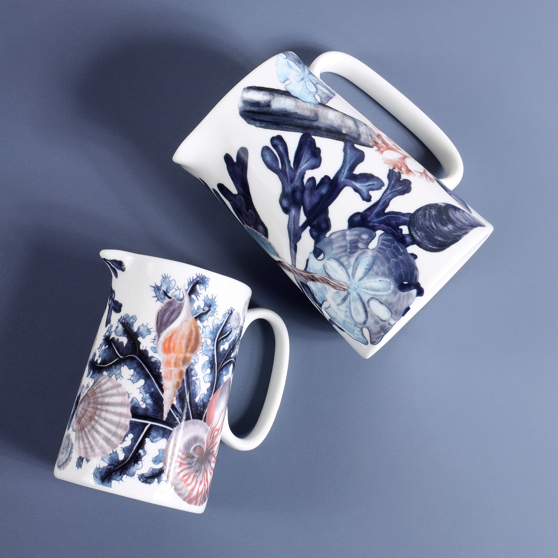 View from above is a Medium size beachcomber jug  showing shades of blue shells,seaweed.Next to it is a small Beachcomber jug decorated with seaweed,scallop and a nautilus shell 