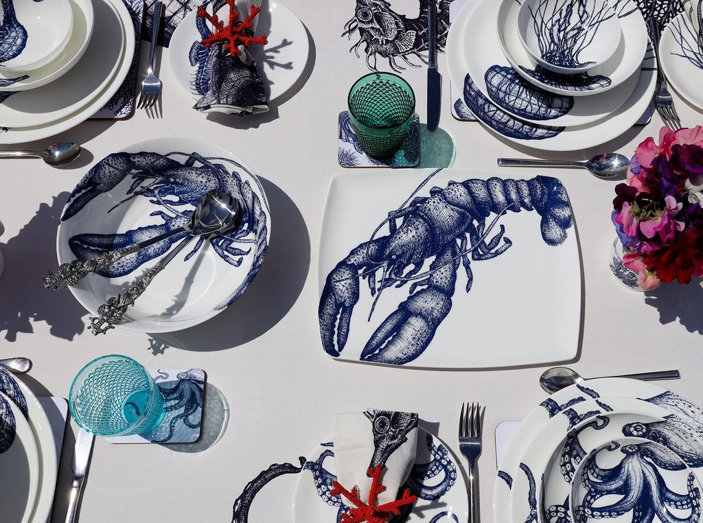 Serving bowl in Bone China in our Classic range in Navy and white in the Lobster design on a white tablecloth.In the bowl are a pair of pewter lobster salad servers,also on the table are other Cream place settings with Dinner plate,side and pasta bowls in Jellyfish and Octopus amongst others