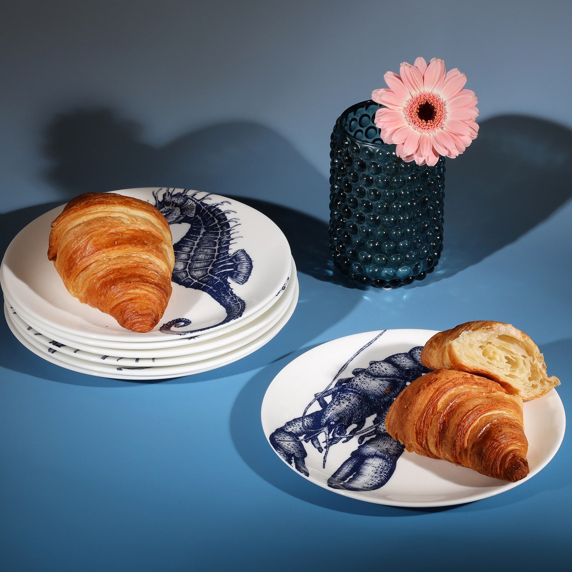 Stacked bone china side plates decorated with croissants next to a petrol blue candle holder