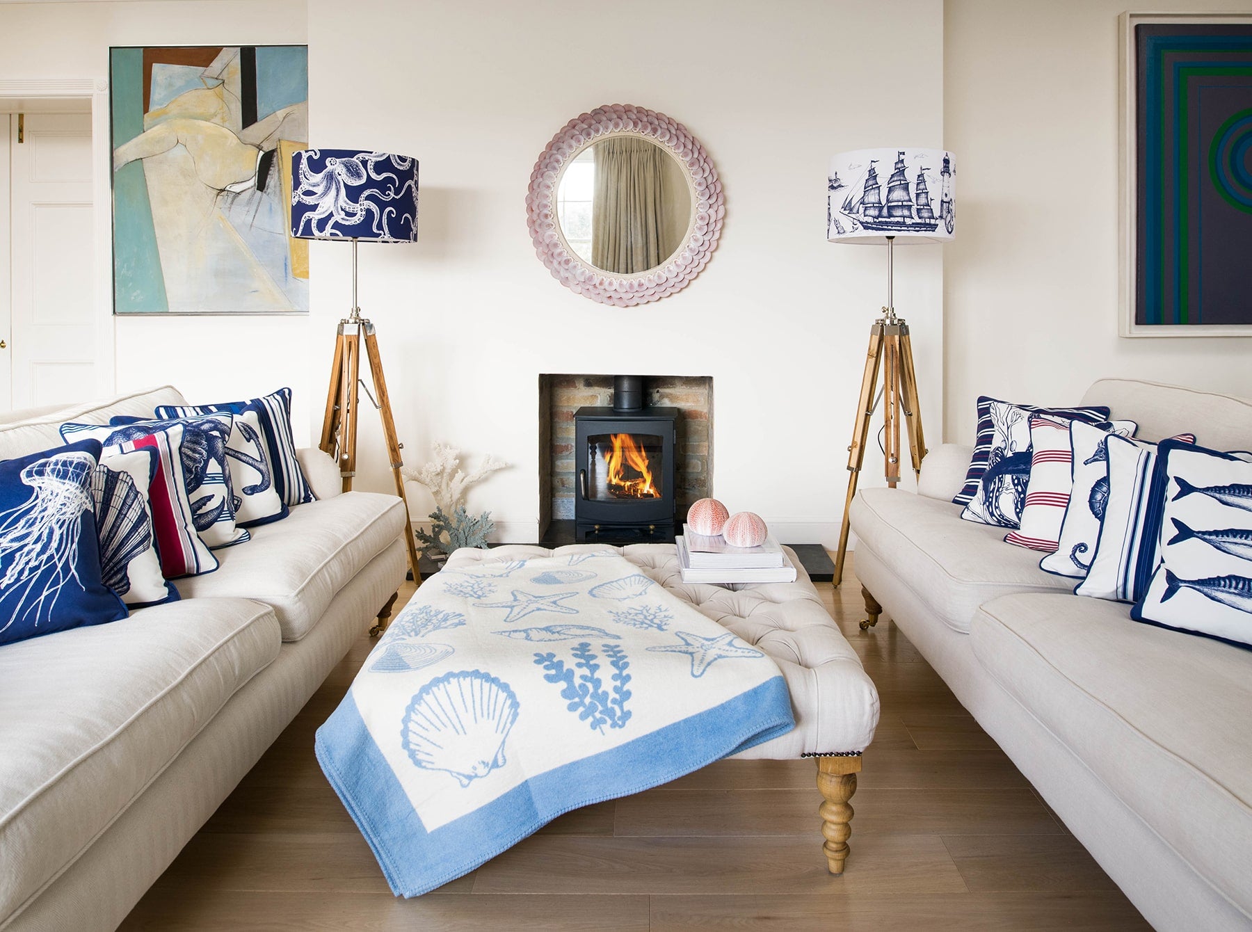 Our Classic Navy Maritime design on a white background on a tripod stand on one side of a fireplace,there is another tripod with a navy octopus lampshade on the other side.In the photo are two large white sofas with our classic cushions placed on them.There is a wood burner in the fireplace and there is a footstool in the middle of the sofas.
