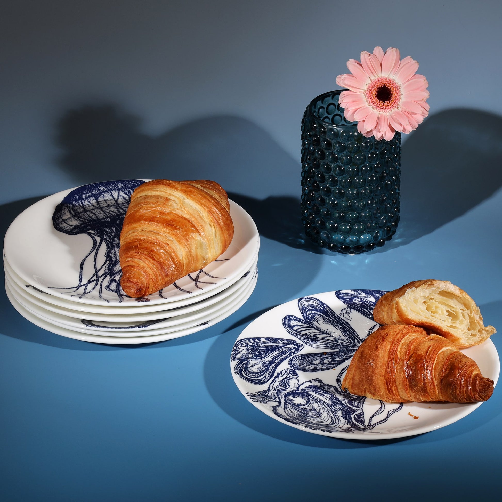 Stacked bone china side plates decorated with croissants next to a petrol blue candle holder